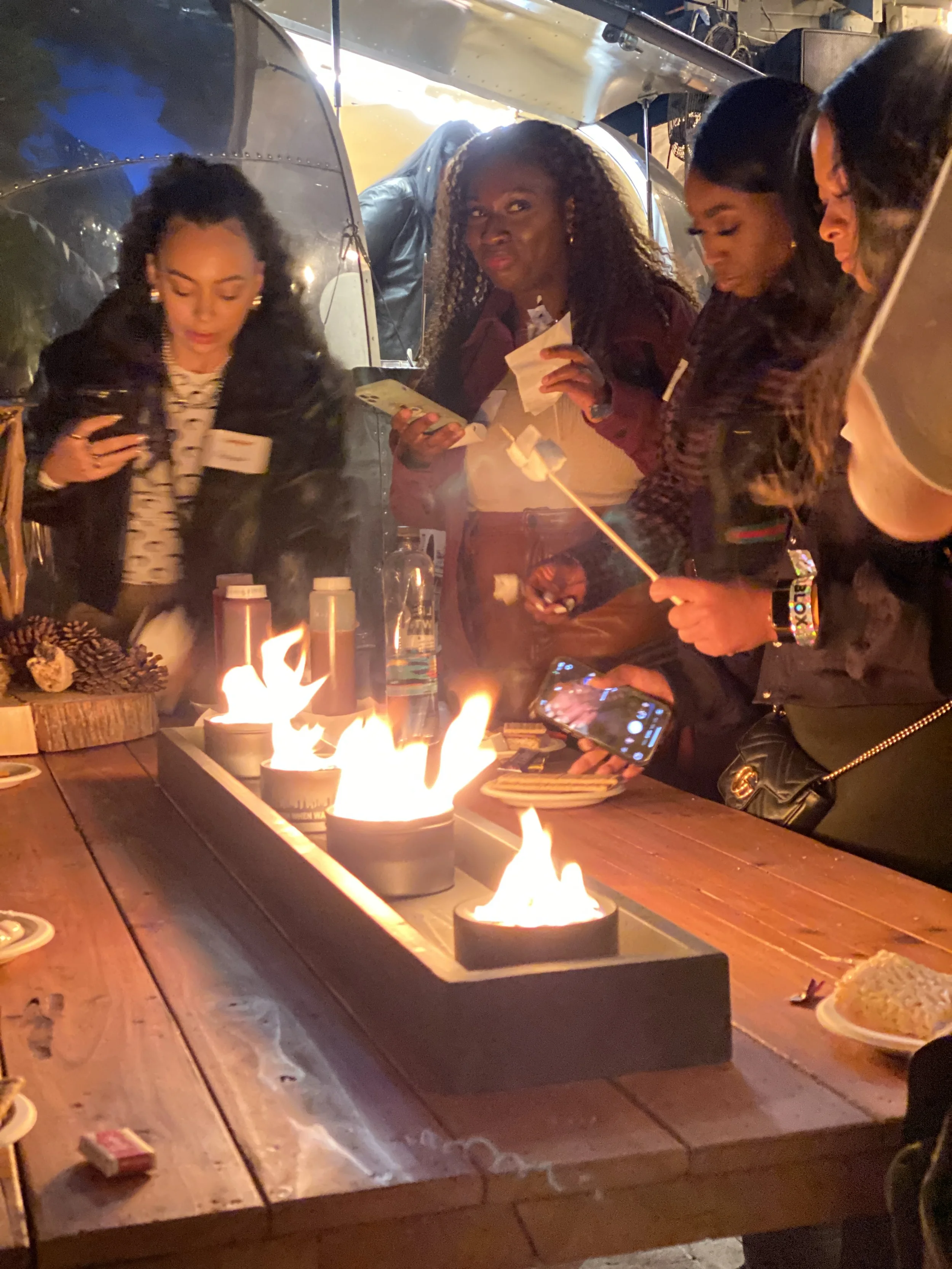 Group of women gathered around a table with small flames, taking photos and looking at a birthday cake with sparklers.