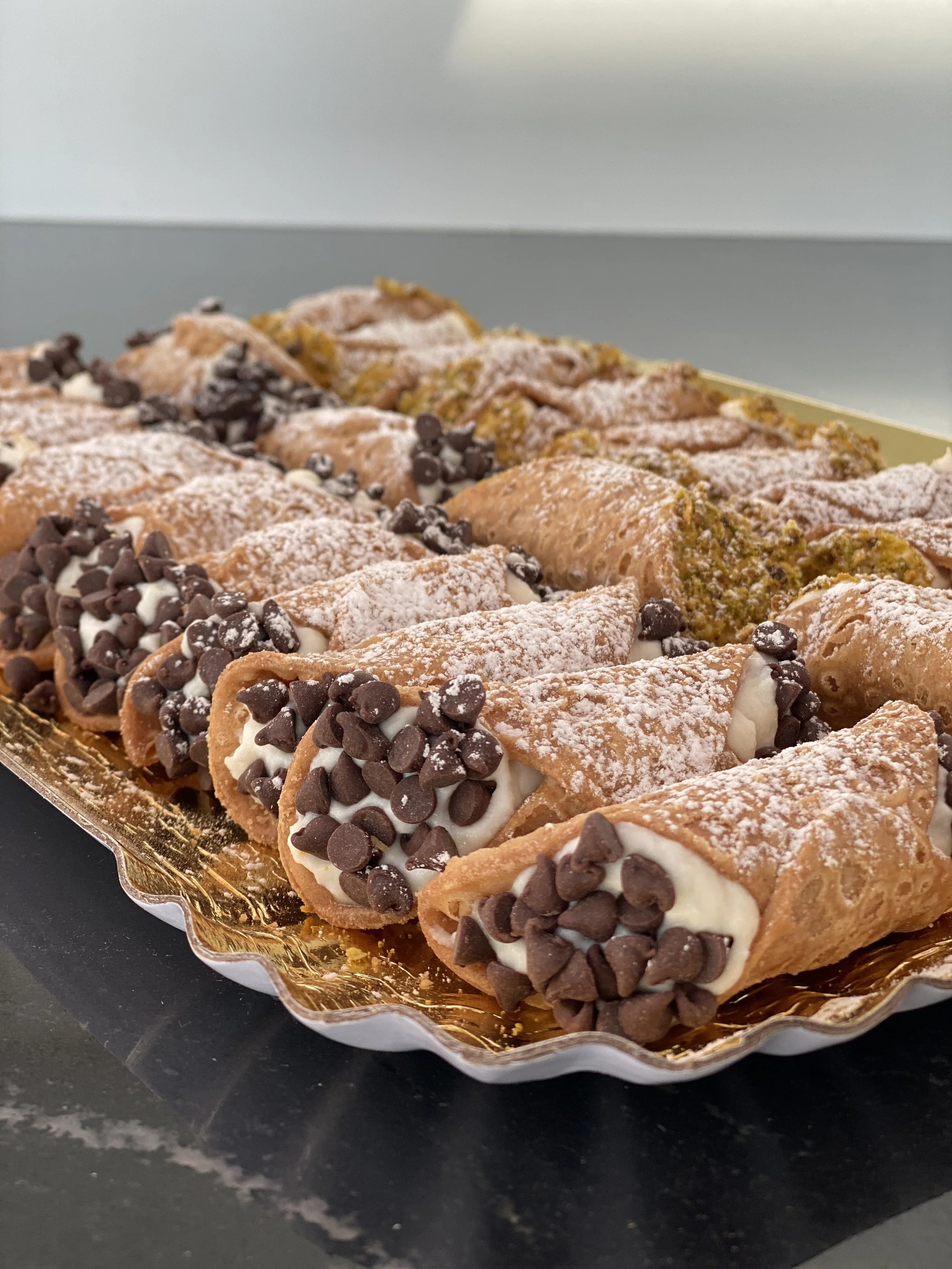 Tray of cannoli filled with cream and topped with chocolate chips, dusted with powdered sugar.