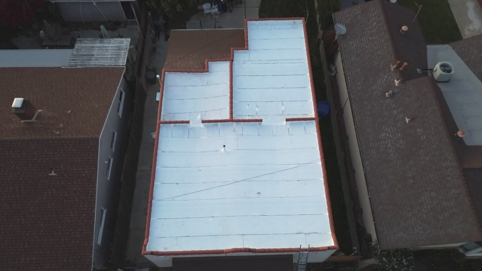 Aerial view of a flat rooftop painted white, surrounded by neighboring rooftops in a residential area.