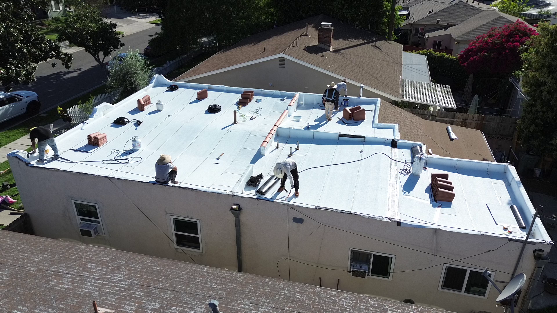 Roofing workers installing a white reflective roof on a building, with some workers applying materials and tools on top.