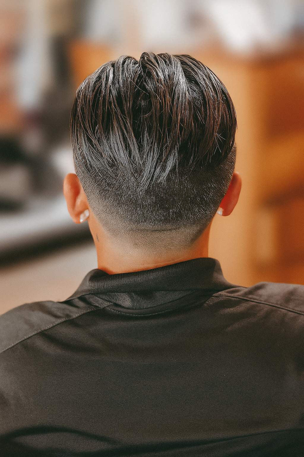 Back view of a person with short, tapered haircut with medium-length, sleek, black hair on top, wearing a black shirt.