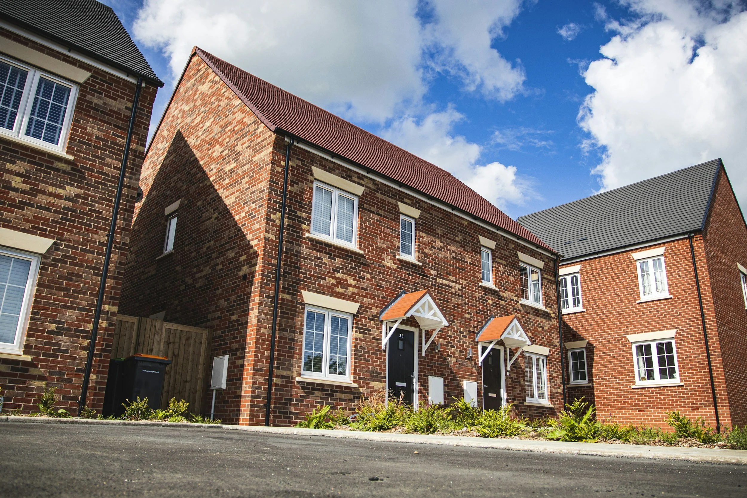 A row of new brick townhouses with white window frames and small front porches, under a partly cloudy blue sky.