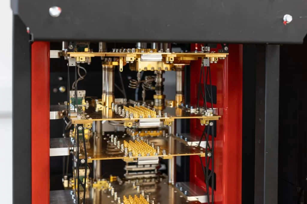 Close-up of a scientific or electronic device with multiple gold-colored circuit boards, wires, and components inside a black and red frame.