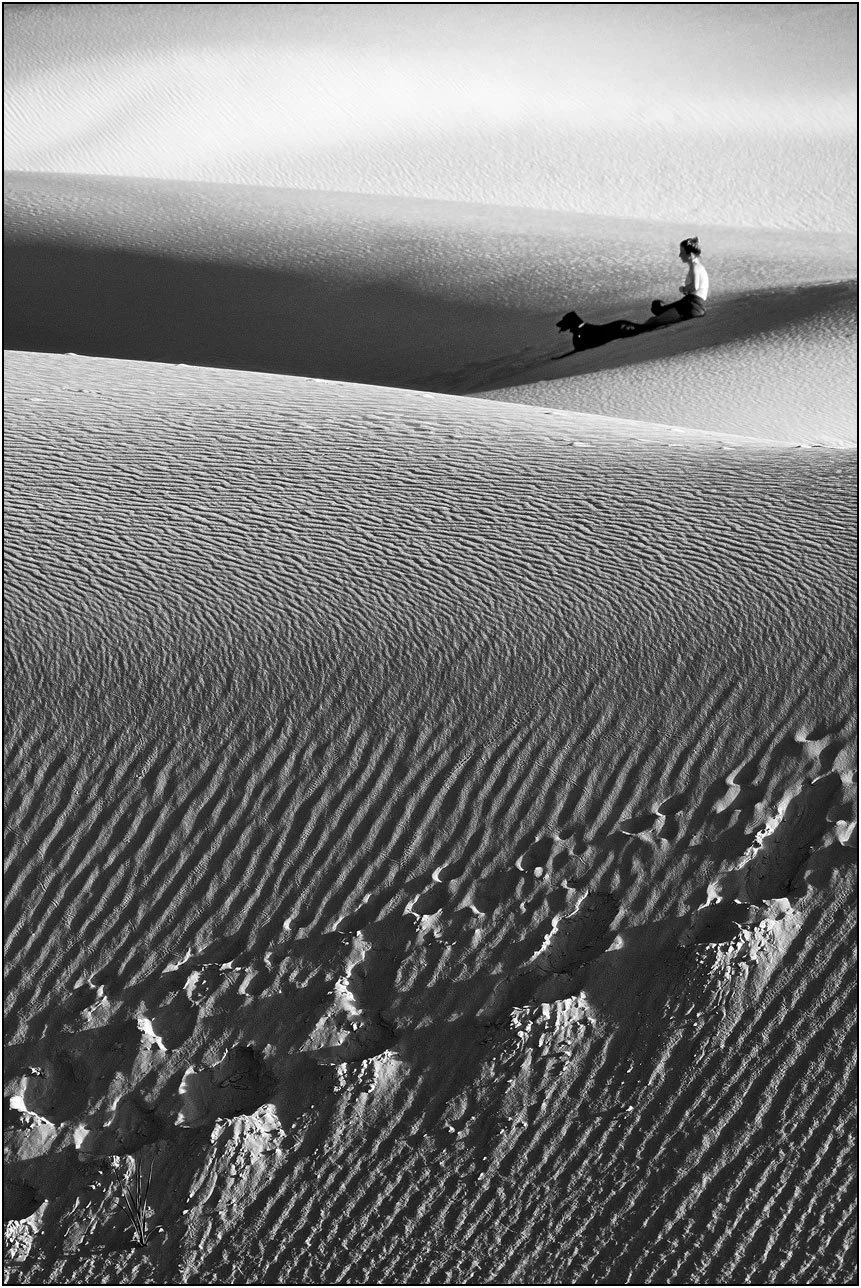 Woman sitting with a dog on rippled sand dunes with footprints in White Sands New Mexico