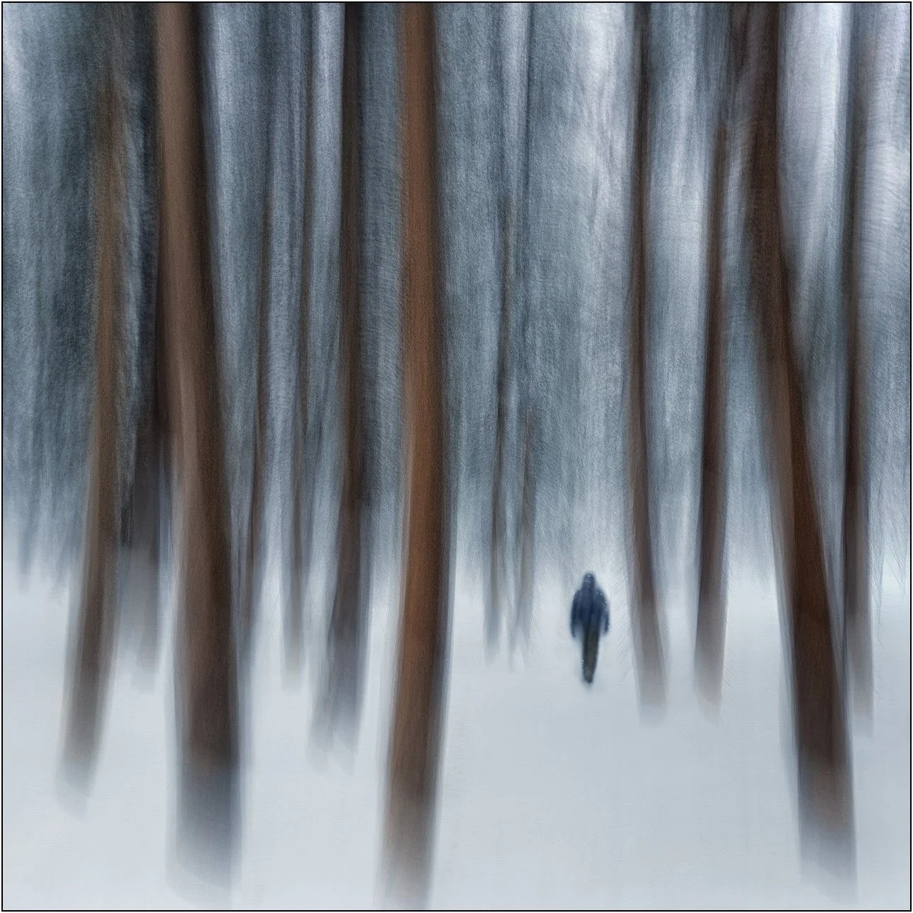 A solitary figure walking through a snowy forest with tall blurred trees