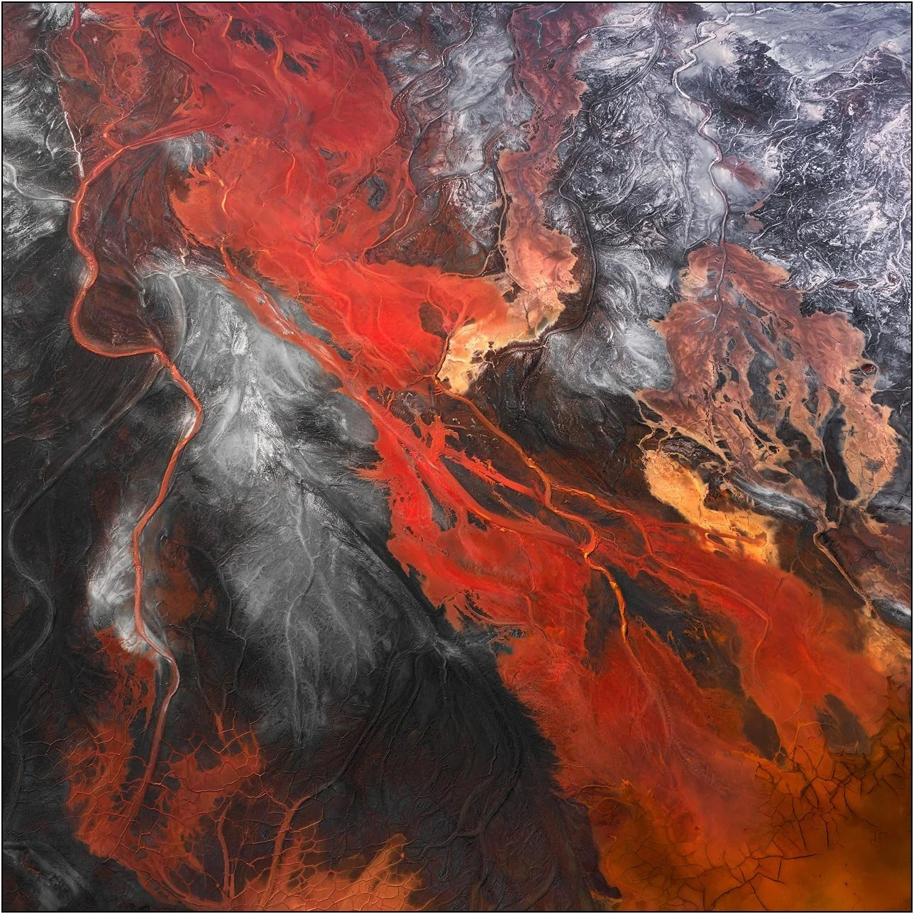 Aerial view of a tailings lake with intense crimson flows cutting through contrasting textures
