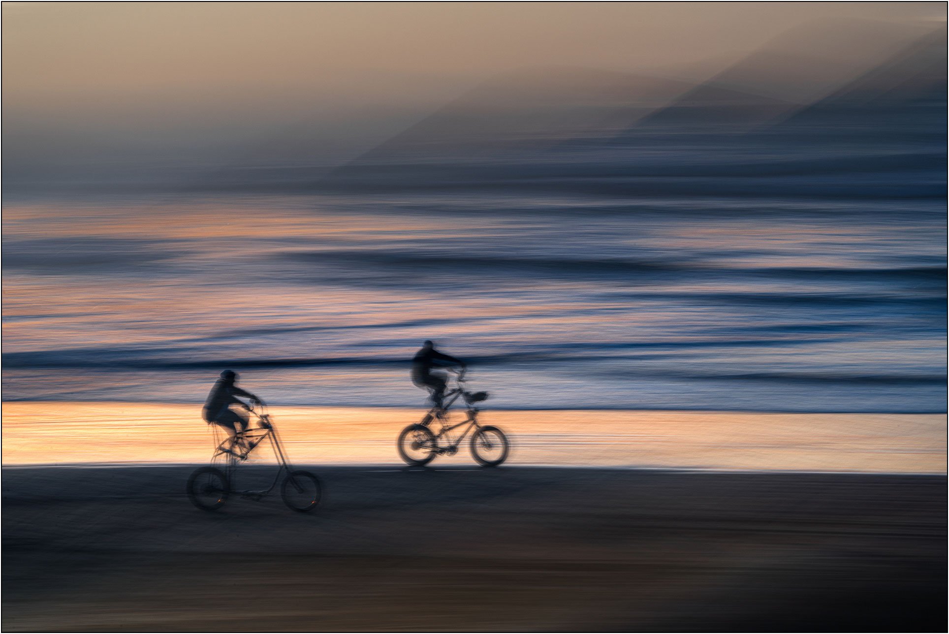 Motion-blurred cyclists riding along the shoreline at sunset, Pismo beach, California.