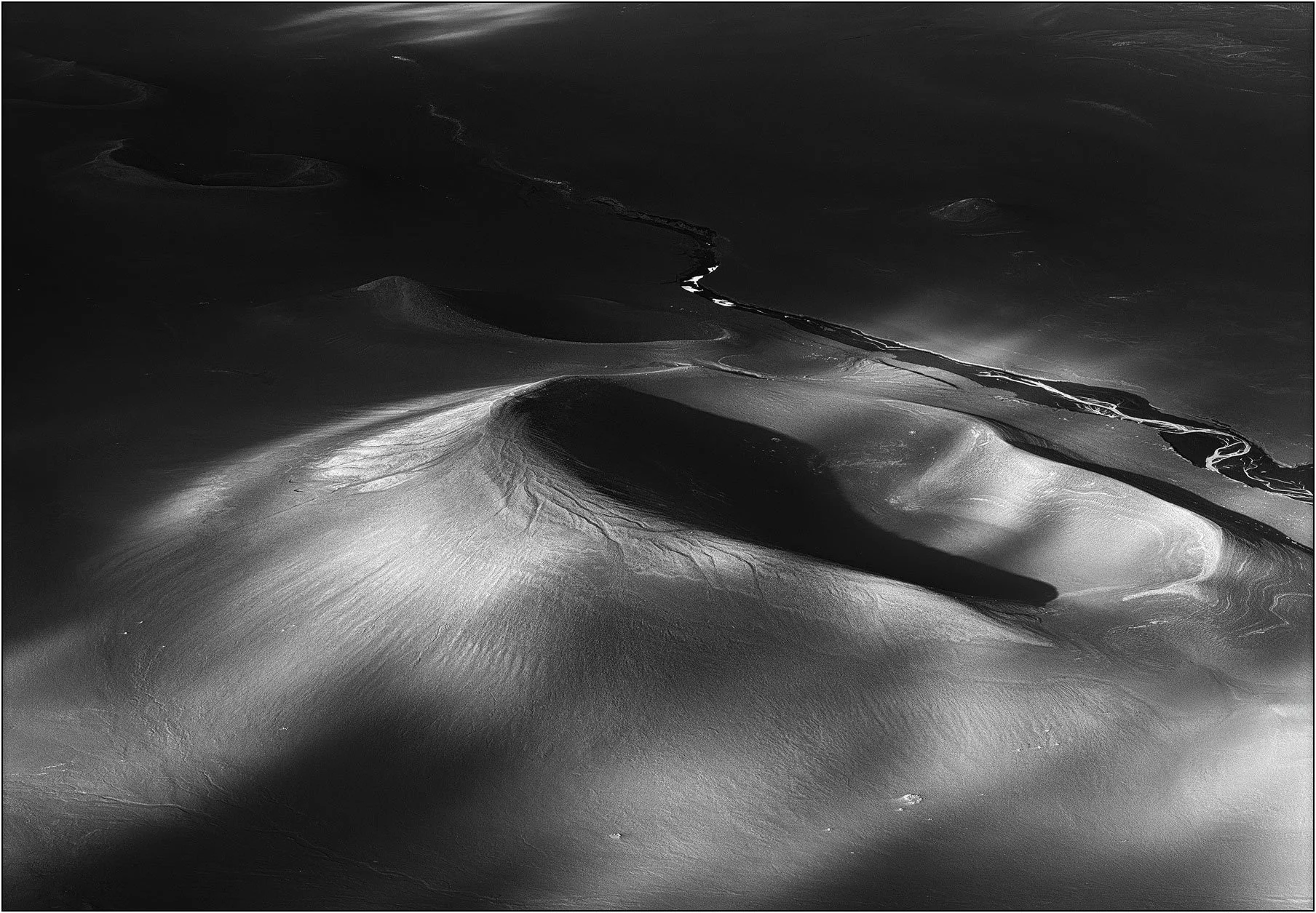 Monochrome aerial view of volcanic sand formations in Iceland, shaped by wind and light into flowing, abstract forms.
