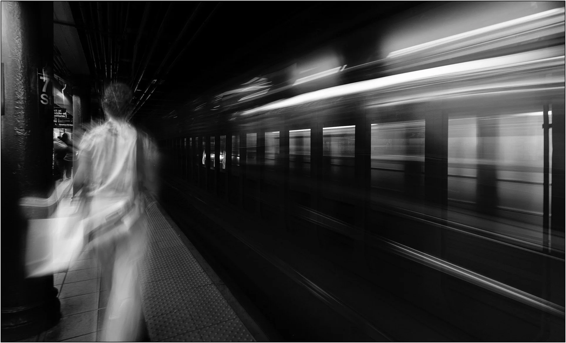 A blurred figure walking along a subway platform as a train rushes past in motion