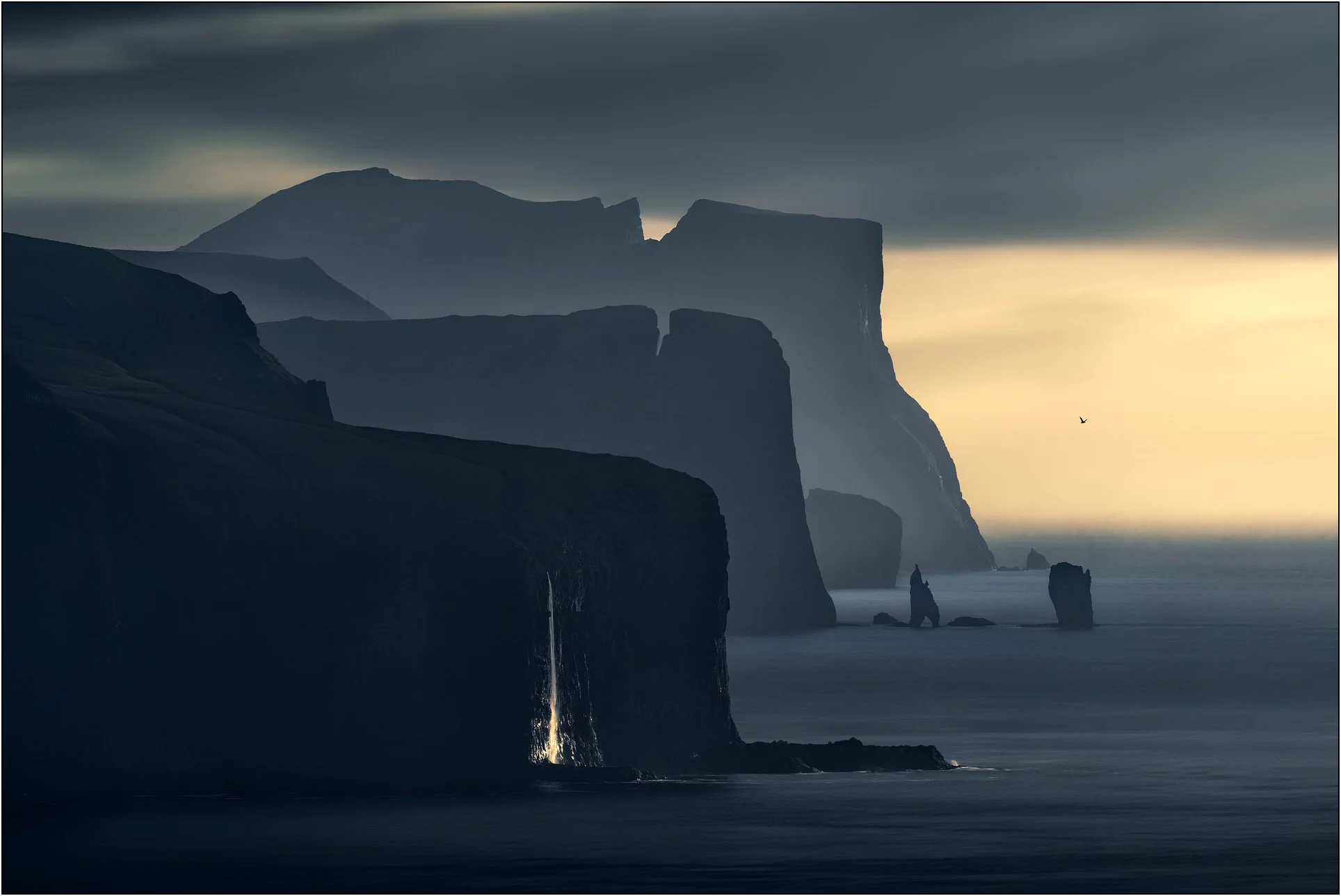 Layers of cliffs and a waterfall at dusk, Kalsoy, Faroe Islands.