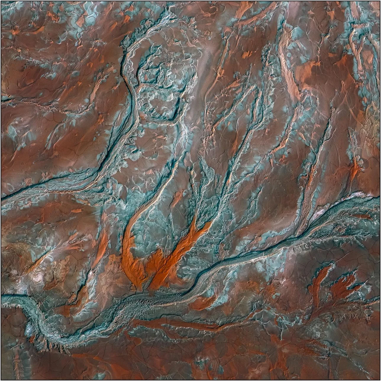 Aerial view of a tailings lake with branching blue-green mineral veins over rust-toned ground