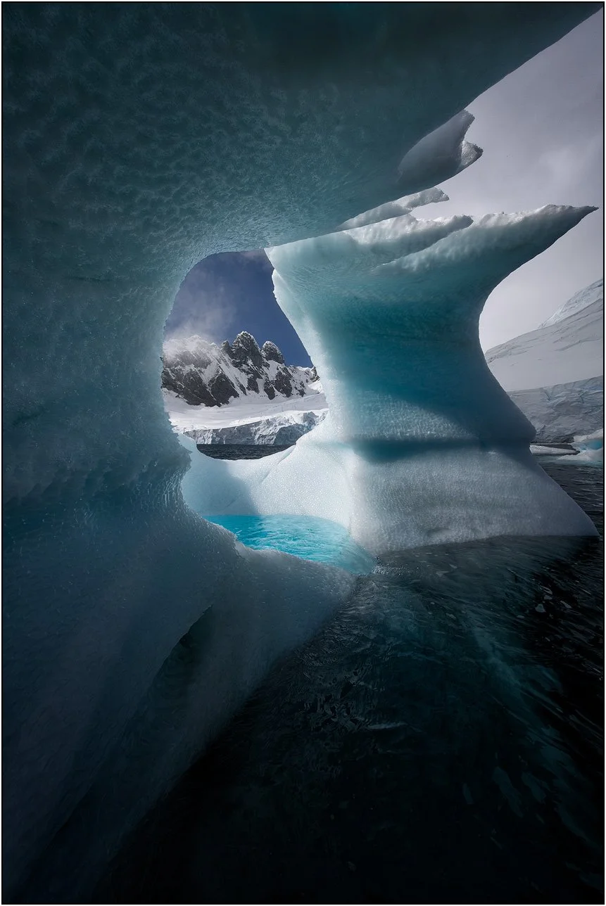 An iceberg arch frames the mountains of Antarctica.