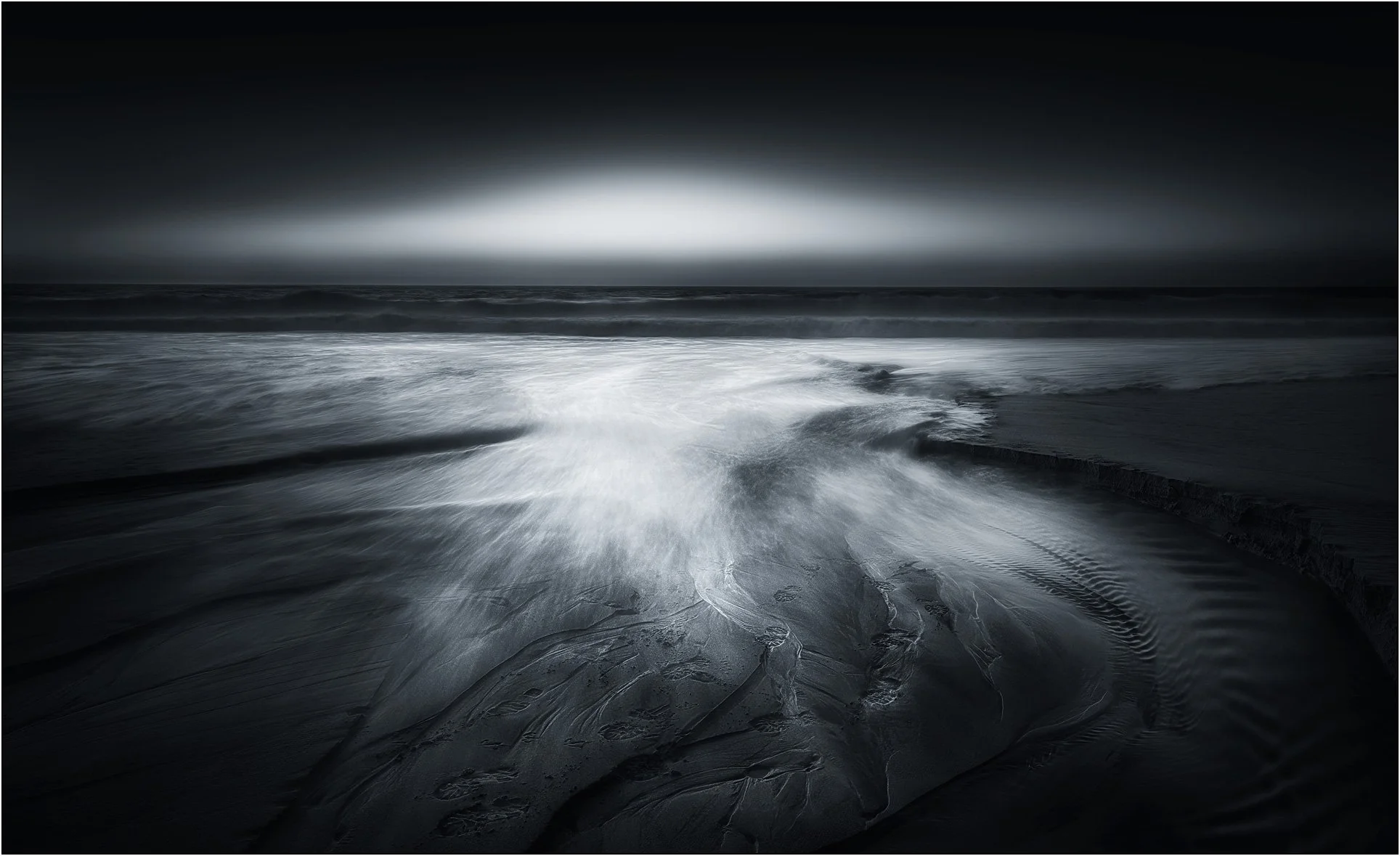 Black and white long exposure of ocean waves flowing across textured sand
