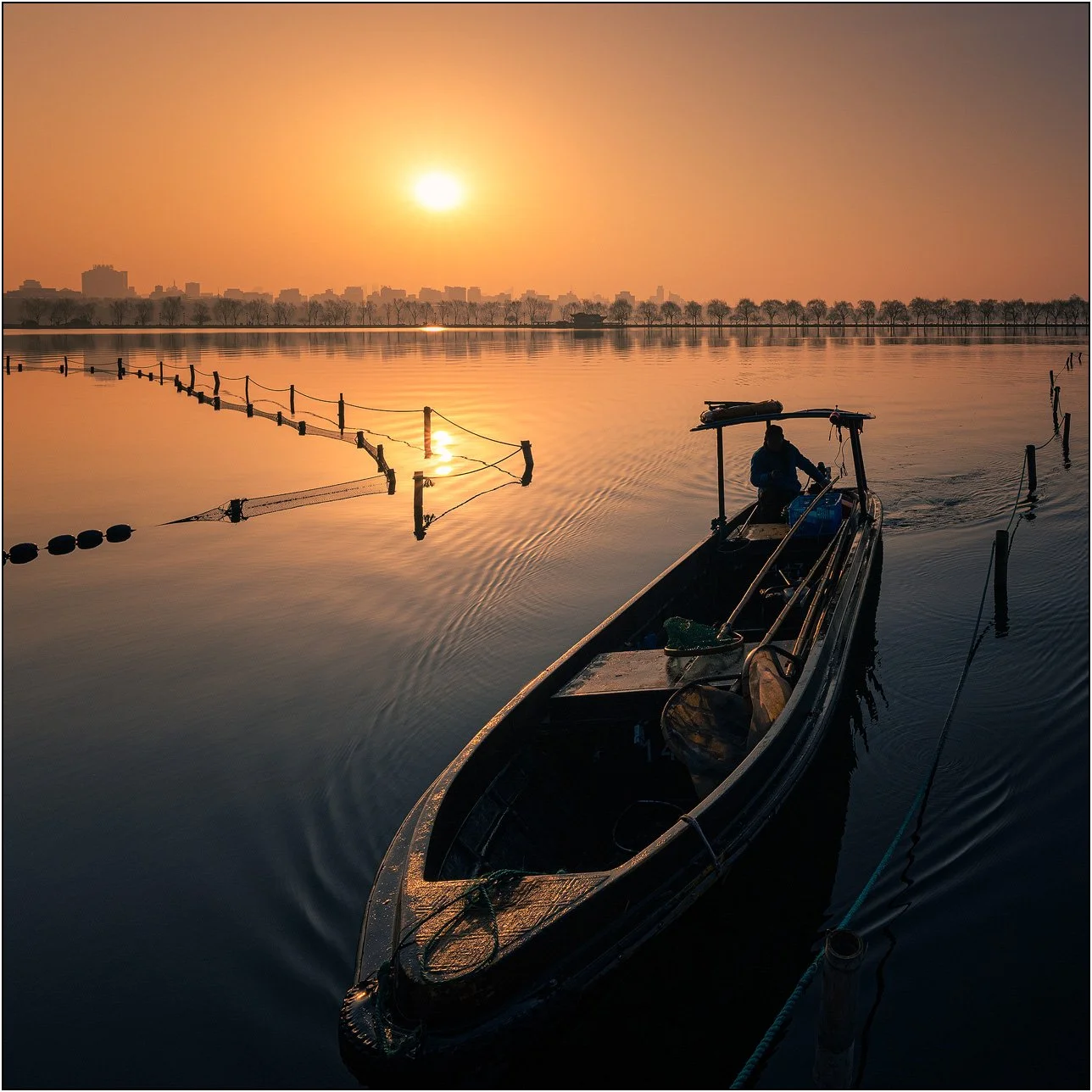 A cleaning worker on boat at sunrise on the West Lake, Hangzhou, China.