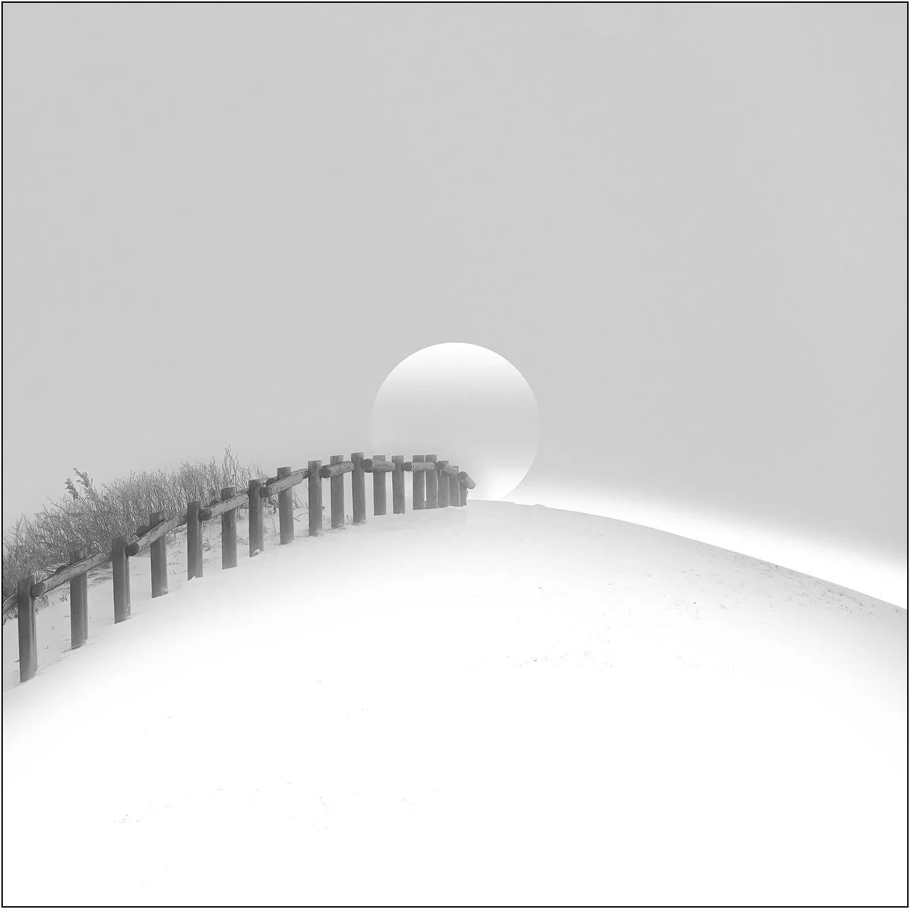 Minimal snowy landscape with a wooden fence leading toward a faint sun in the mist, Hokkaido, Japan.