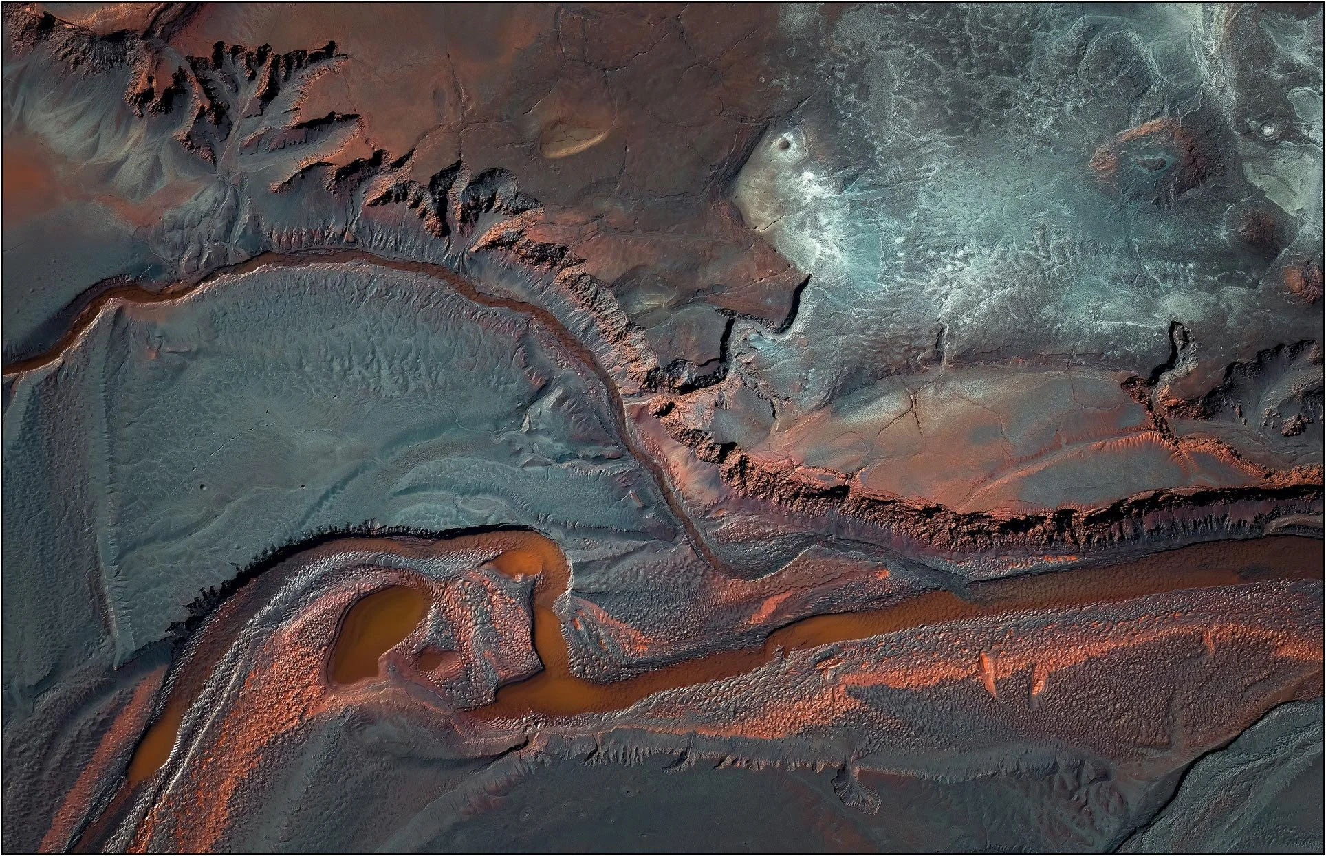 Aerial view of a tailings lake with winding channels and sculpted sediment ridges