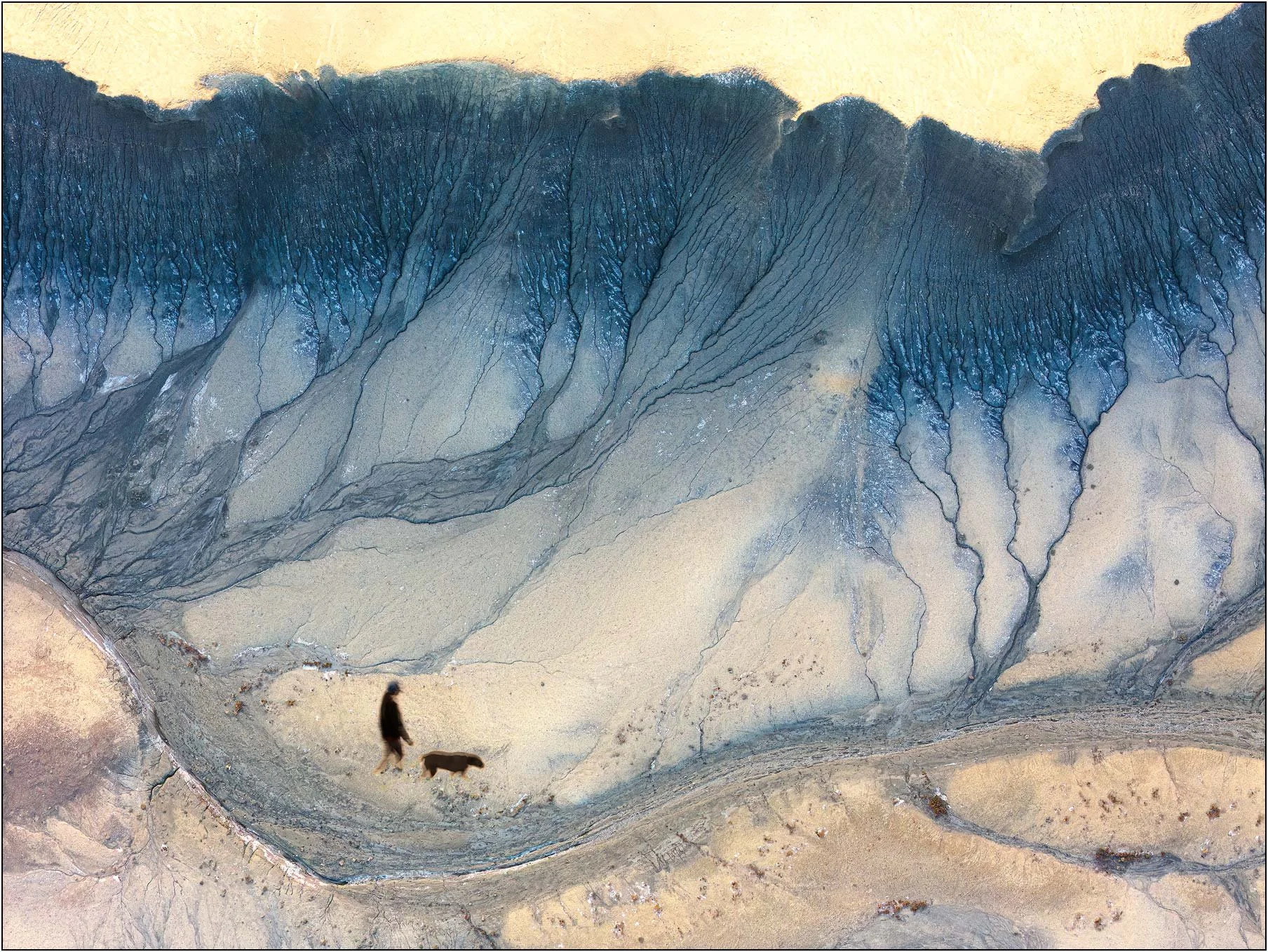 Aerial landscape with a person walking a dog across abstract badlands terrain in Utah