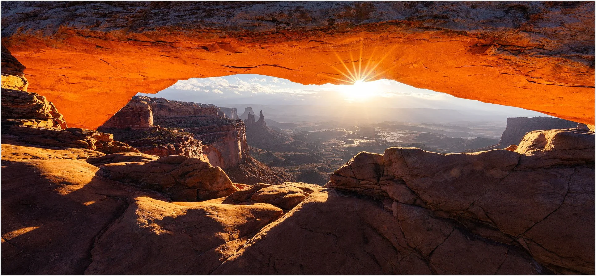 Sunrise through mesa arch overlooking a canyon landscape in Canyonland national park