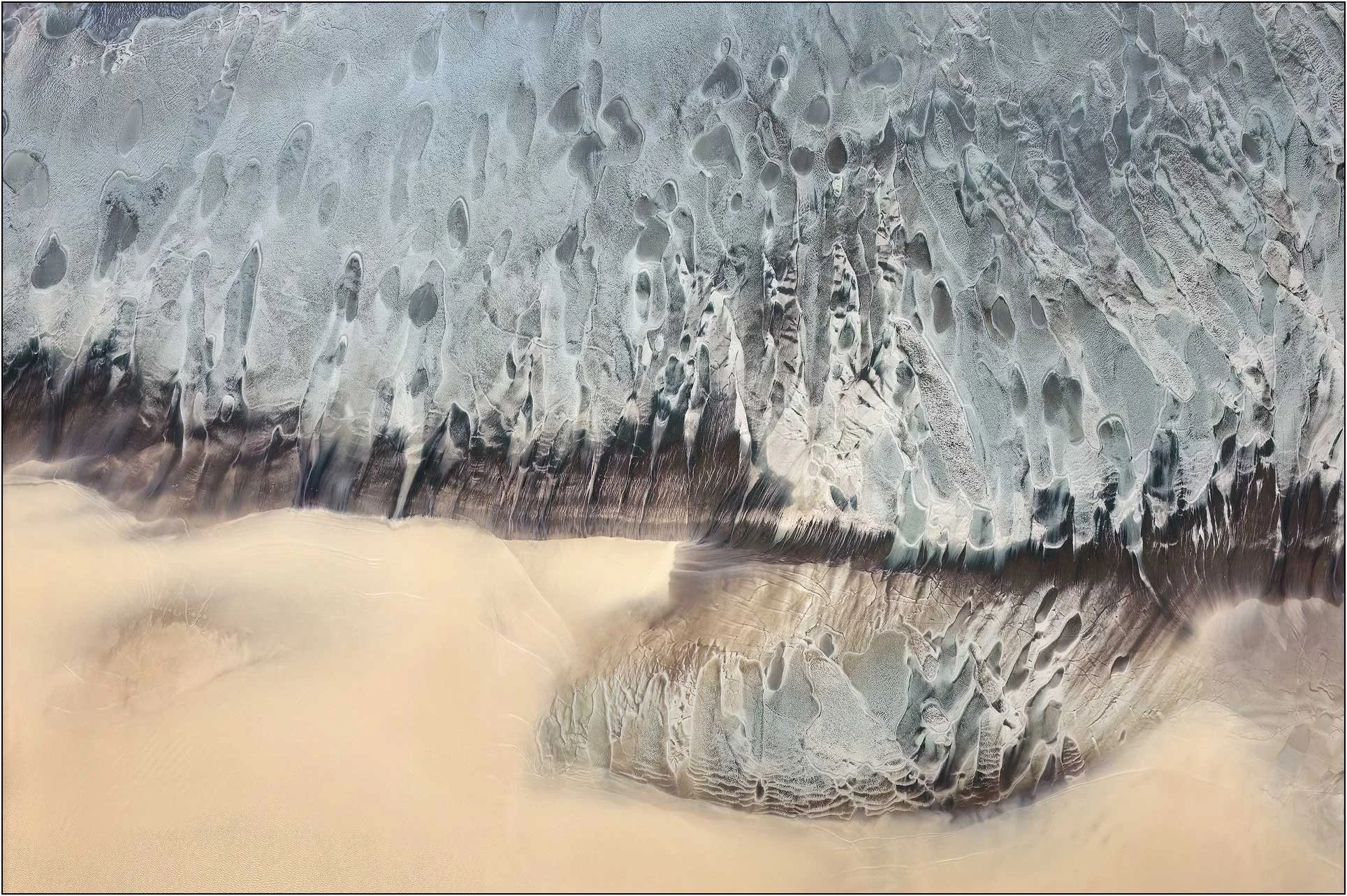 Abstract aerial photography of the Qiantang River tidal flats in China, where tides sculpt sand and sediment into delicate organic patterns. Pale blue-gray textures meet warm expanses of sand, creating an otherworldly landscape reminiscent of melting
