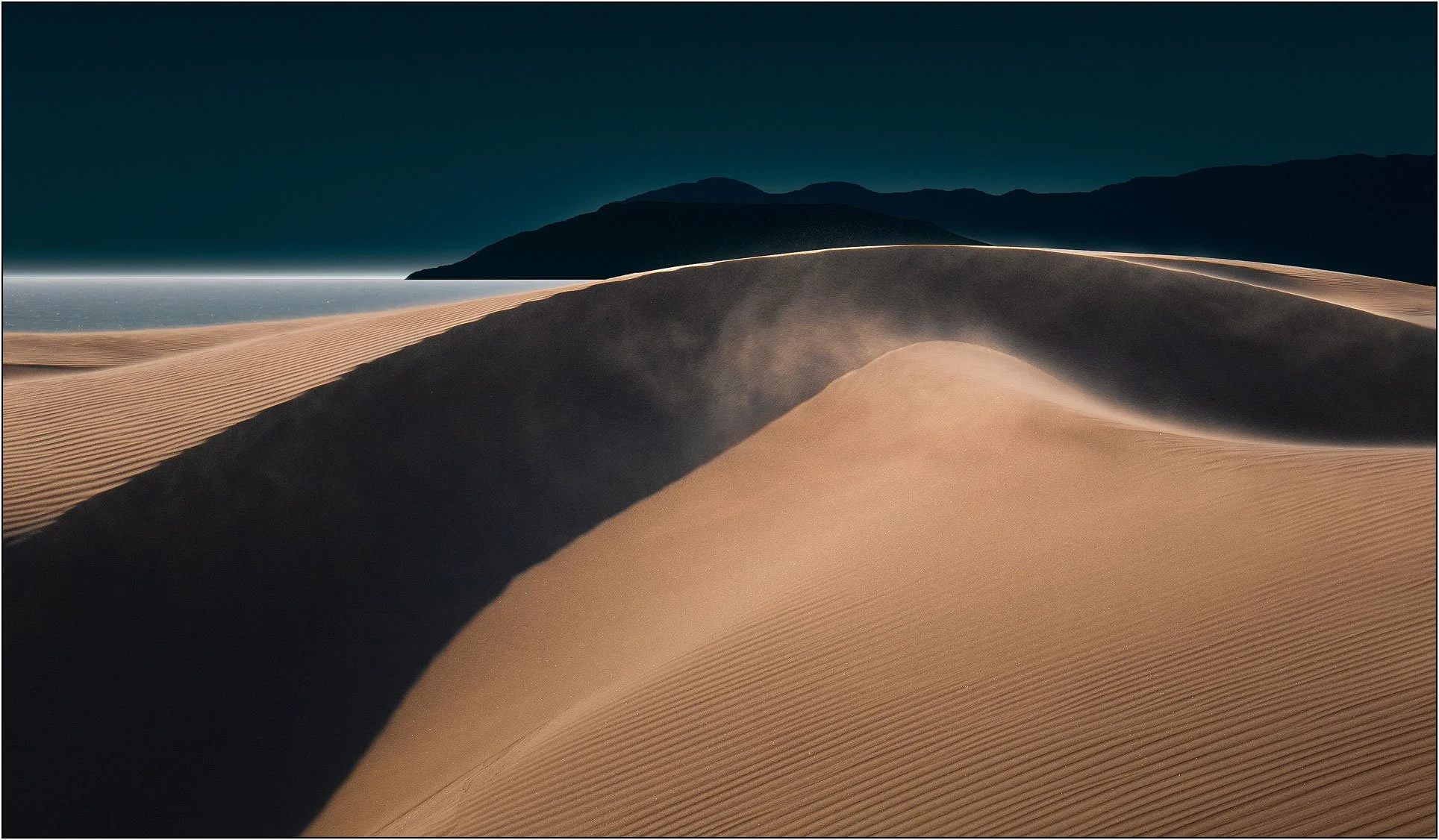 Wind-shaped sand dunes with soft light and distant mountains