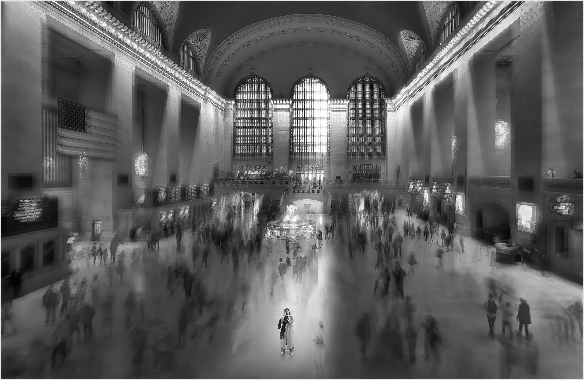 Blurred crowd moving through Grand Central Terminal in New York with a solitary figure standing still at the center
