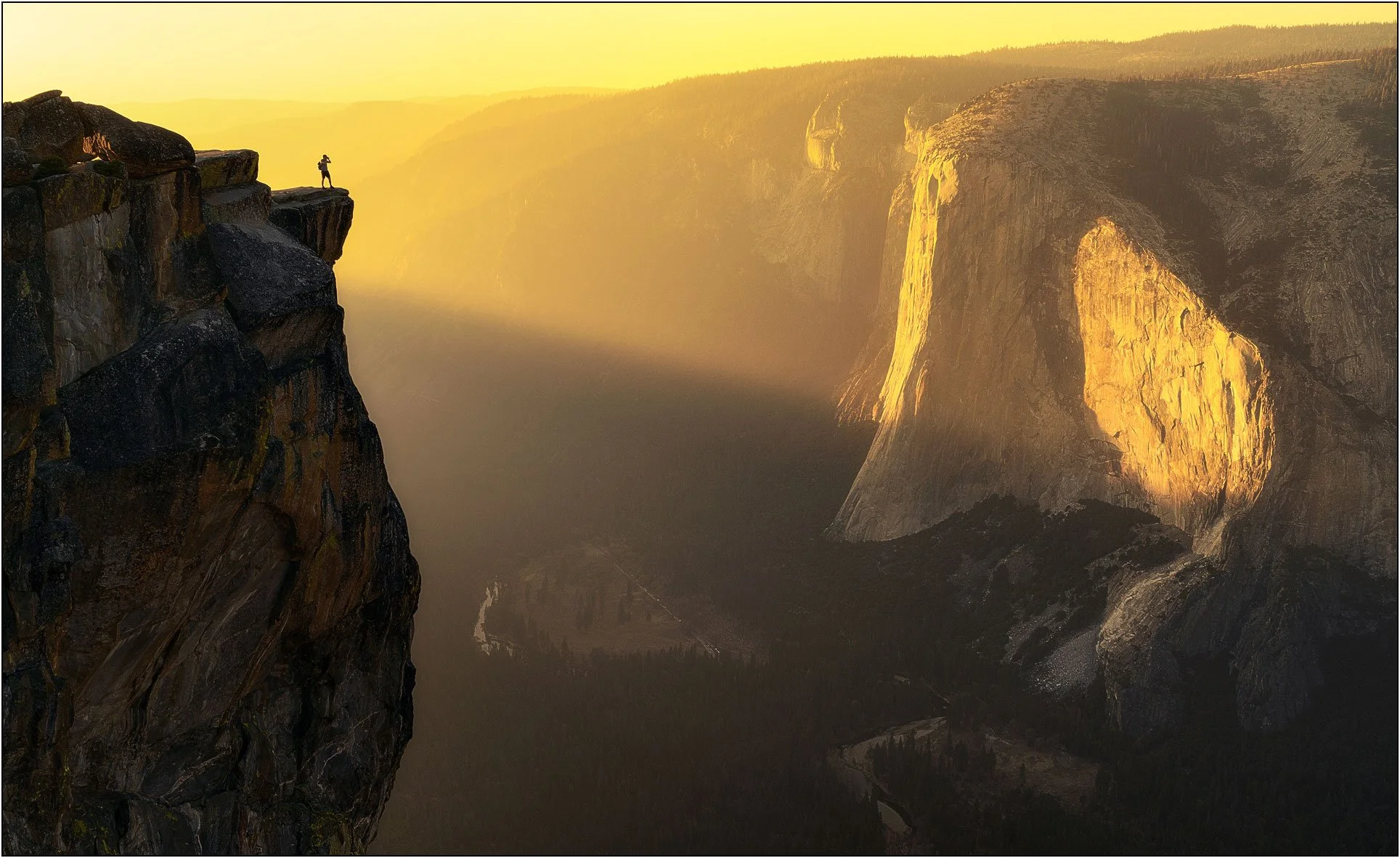 Photographer standing on a cliff overlooking Yosemite Valley at sunset with golden light on Taft Point