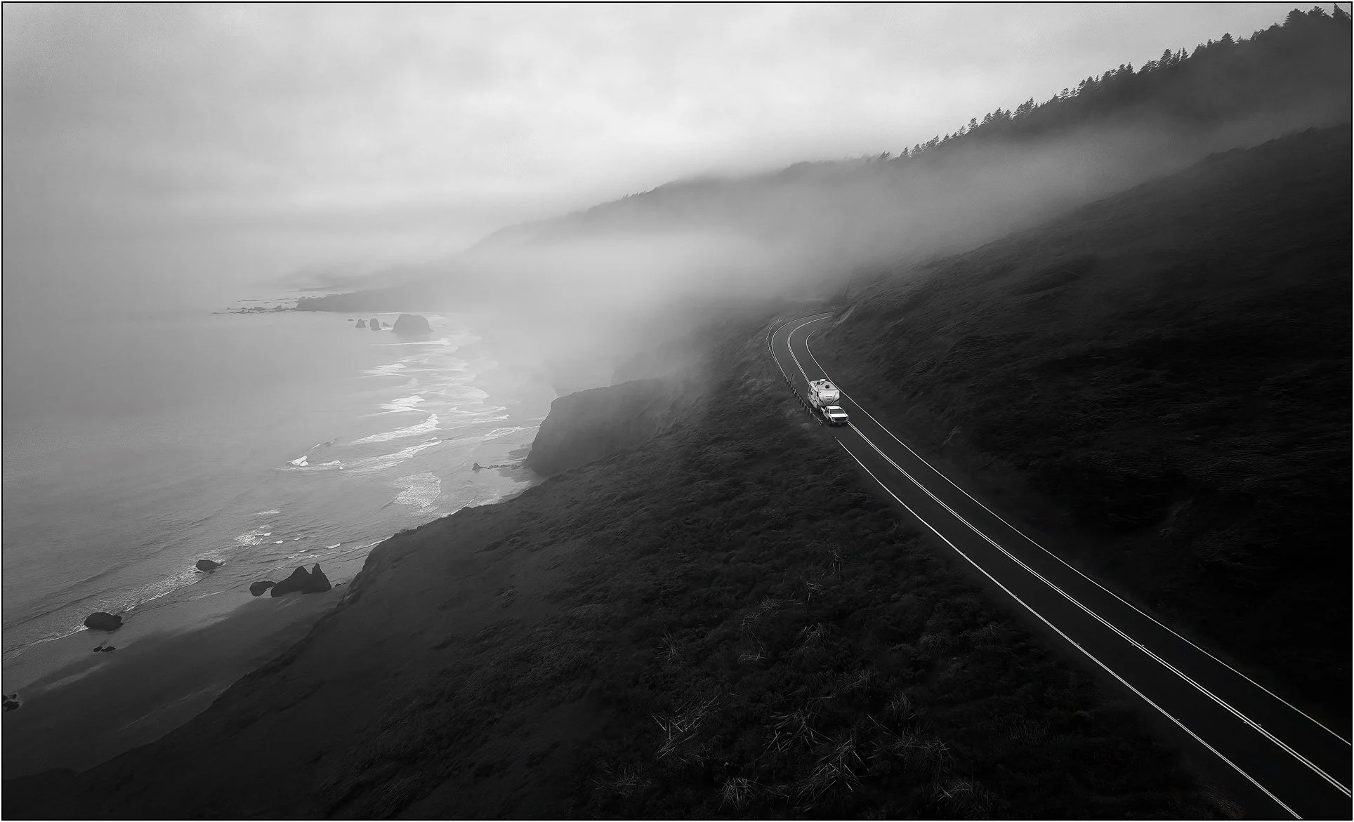 Foggy coastal highway winding along cliffs with a lone vehicle above the ocean