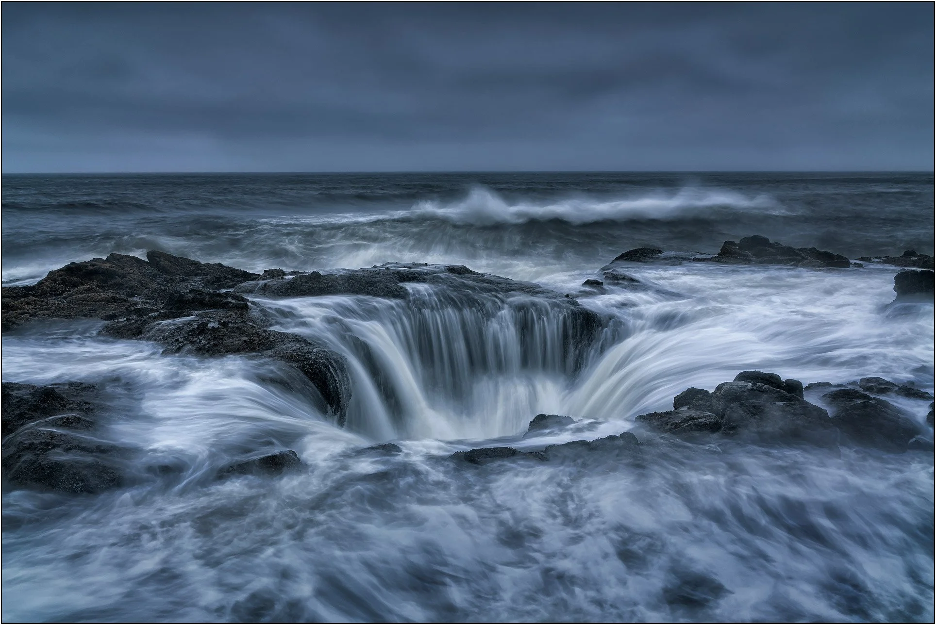Waves cascading into a coastal sinkhole under stormy skies, Thor's Well, Oregon.
