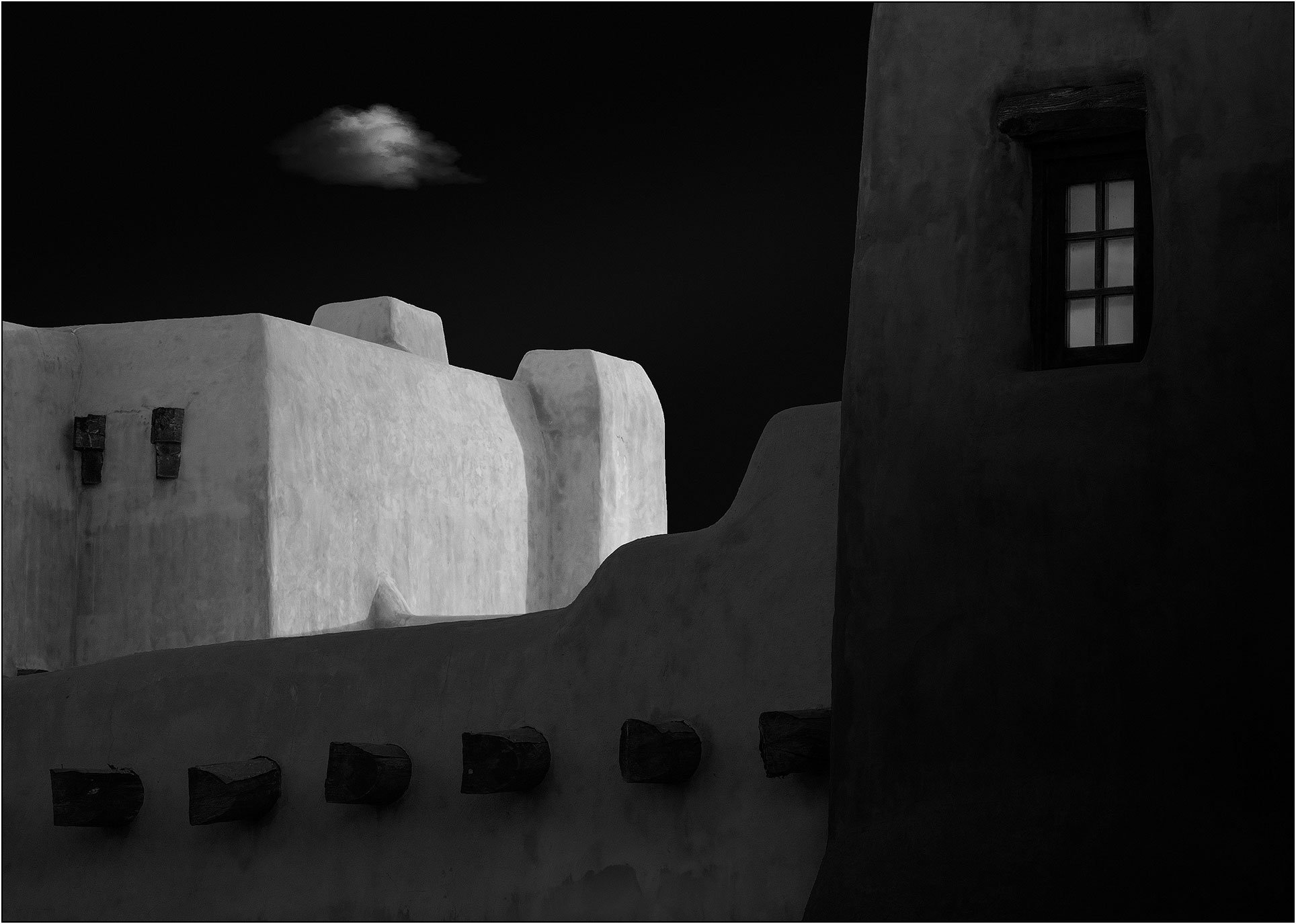 Minimalist adobe architecture in black and white with a single cloud