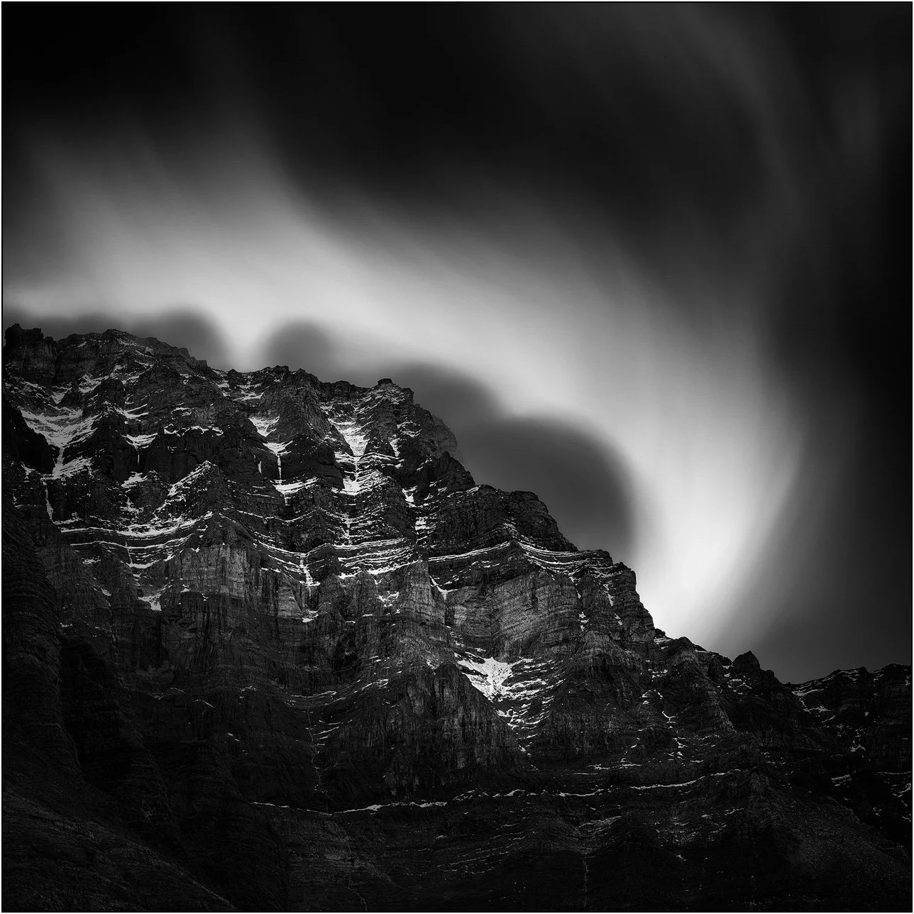 Black and white long exposure photograph of cloud and peaks of the Canadian Rockies.
