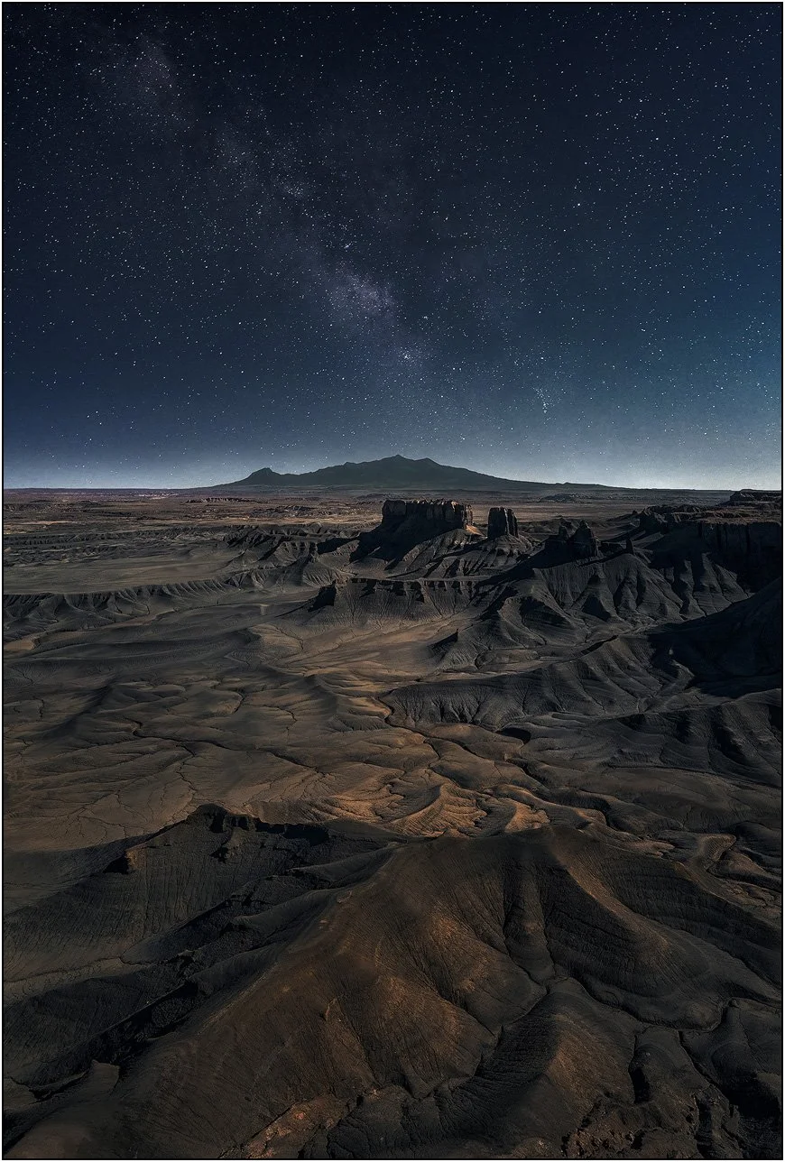 Milky Way rising above a vast desert landscape with rugged rock formations