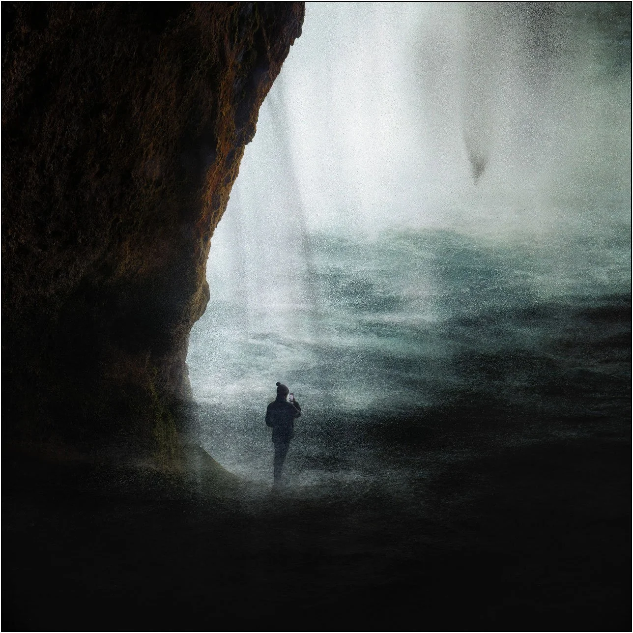 A solitary figure behind Seljalandsfoss waterfall, captured through layered exposures with mist and flowing water.