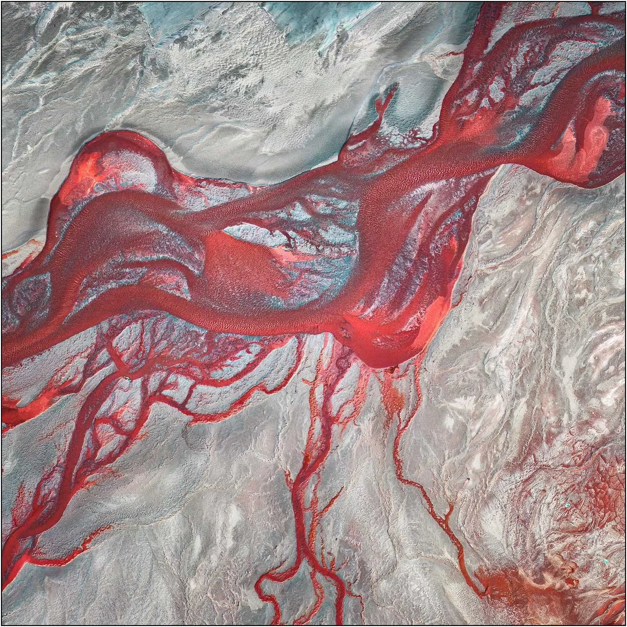 Aerial view of a tailings lake with vivid red channels spreading across pale sediment
