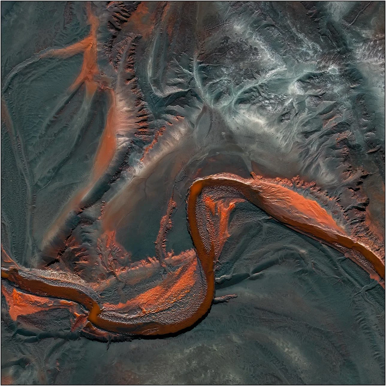 Aerial view of a tailings lake with a winding mineral channel cutting through layered sediment