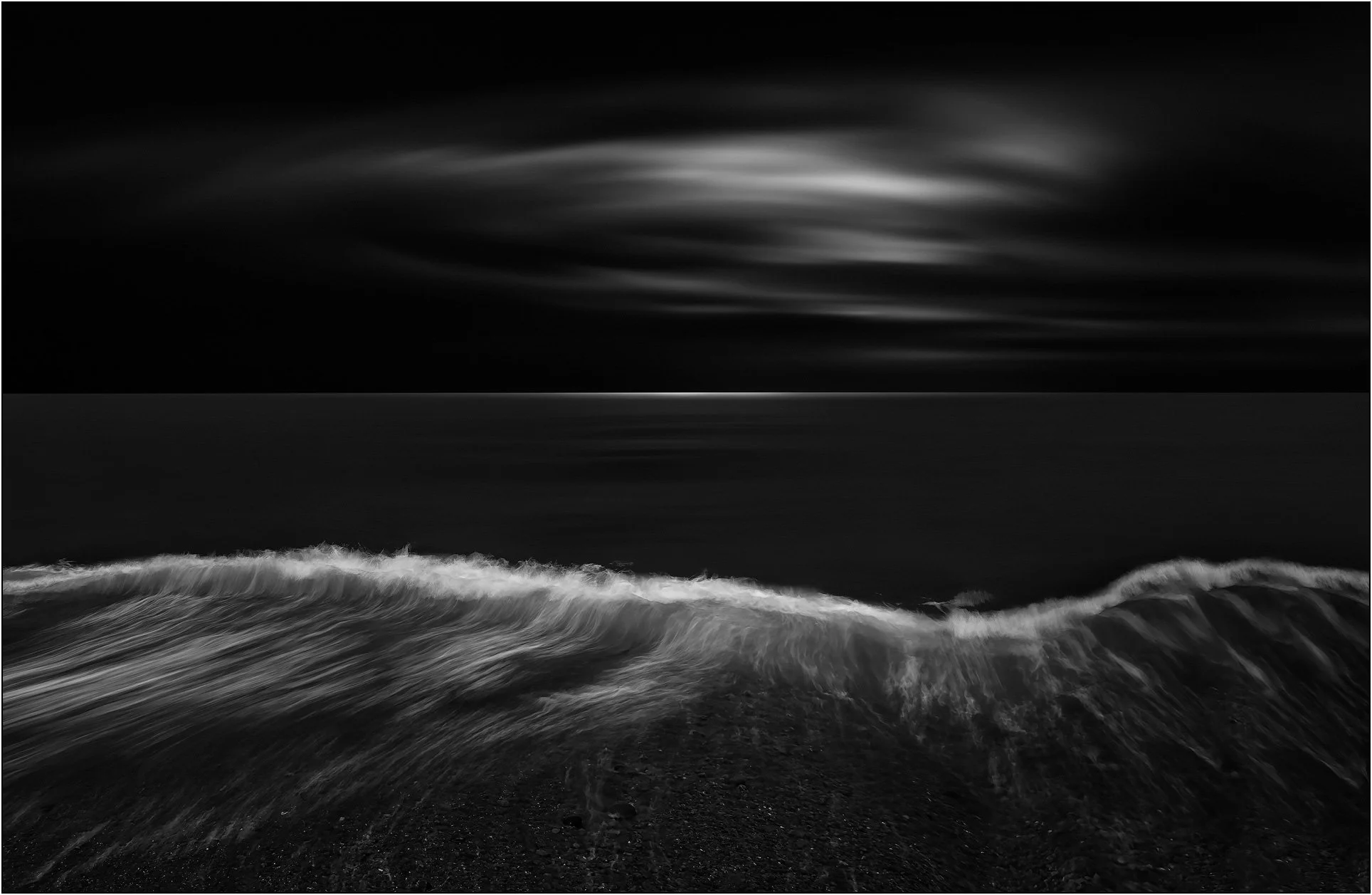 Minimalist black and white seascape with long exposure waves converging toward light under soft clouds