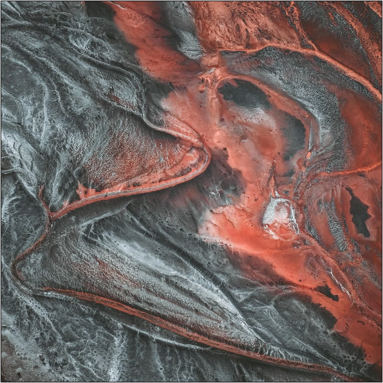 Aerial view of a tailings lake with deep red and charcoal patterns forming layered structures