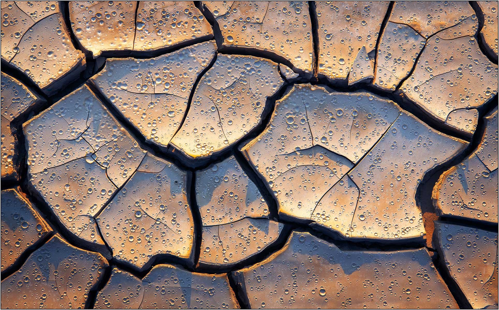 Close-up of cracked mud with water droplets and warm light tones