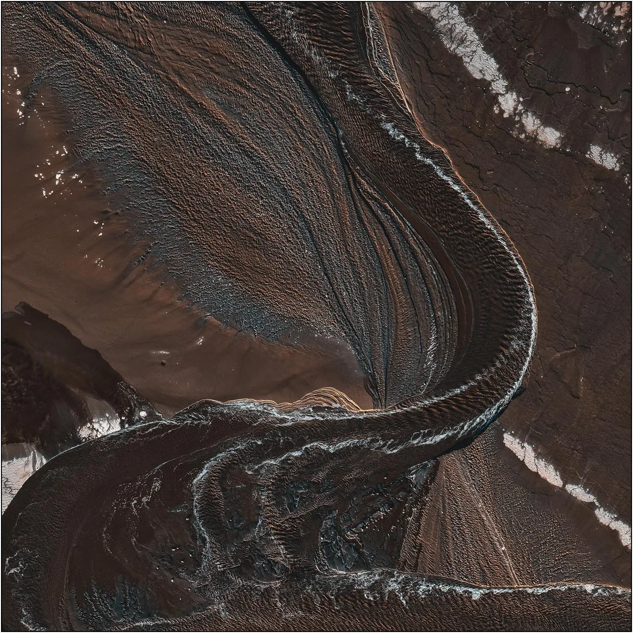Aerial view of a tailings lake with a winding channel cutting through fine textured sediment