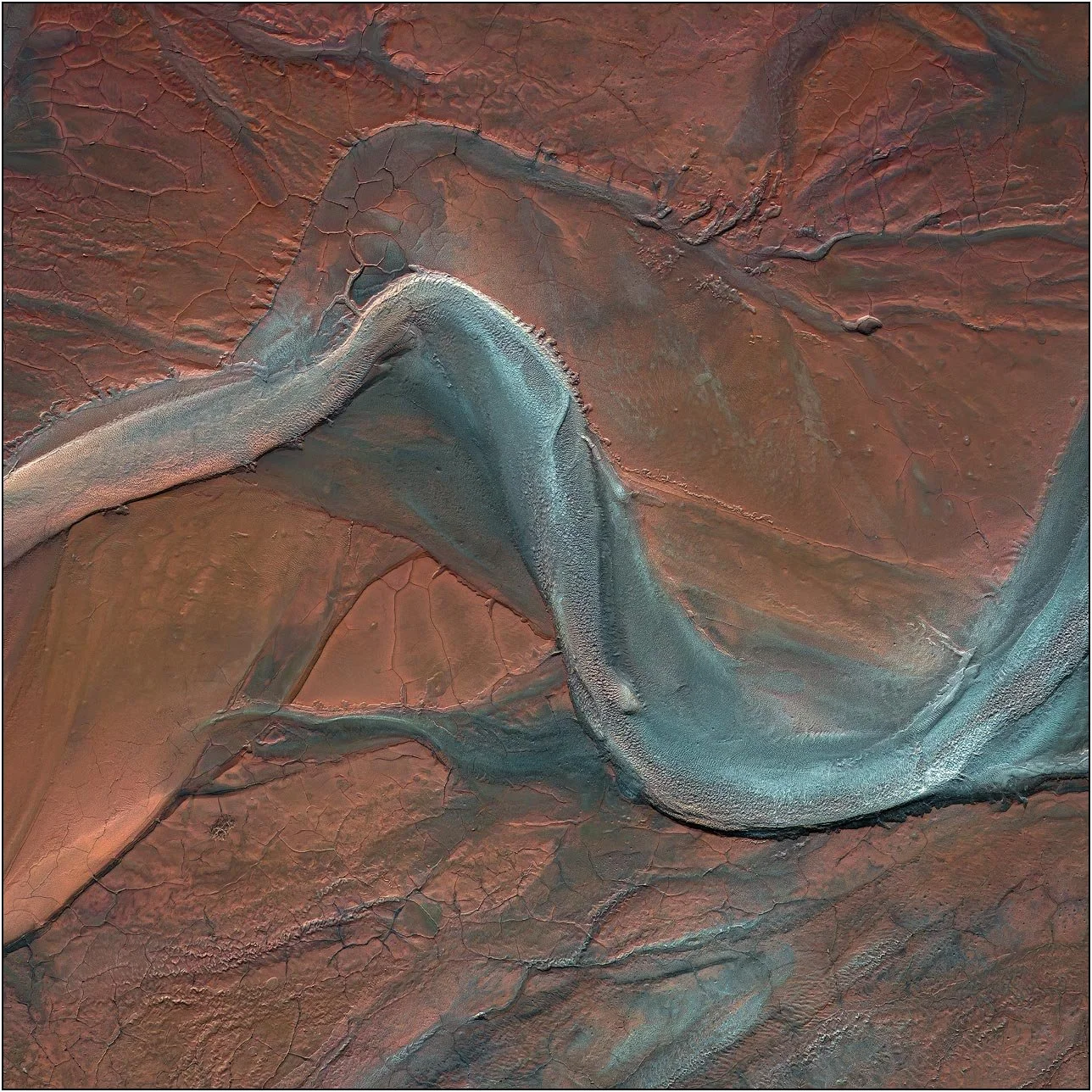 Aerial view of a tailings lake with a smooth serpentine form across cracked earth patterns