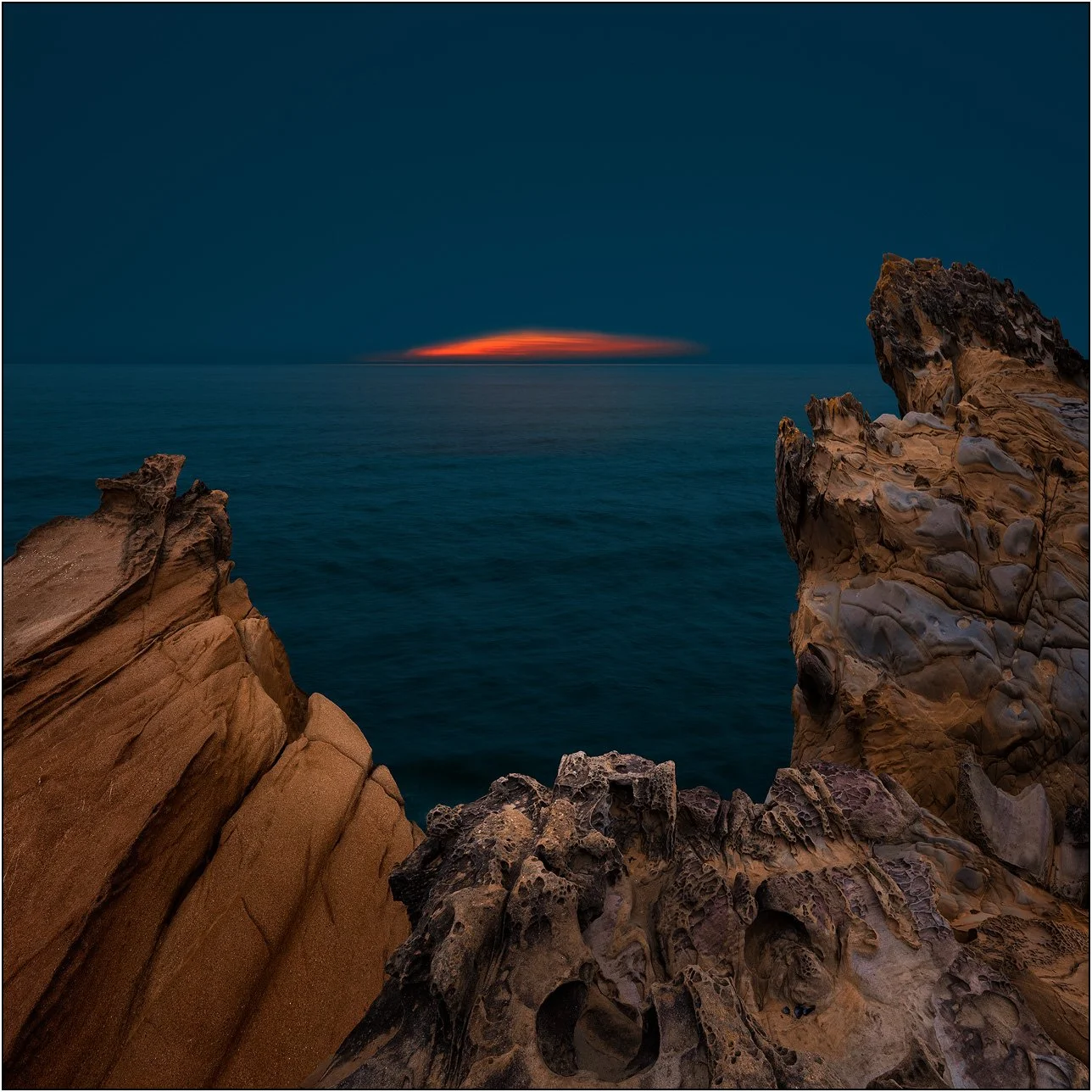 Minimal seascape framed by sculpted coastal rocks at sunset