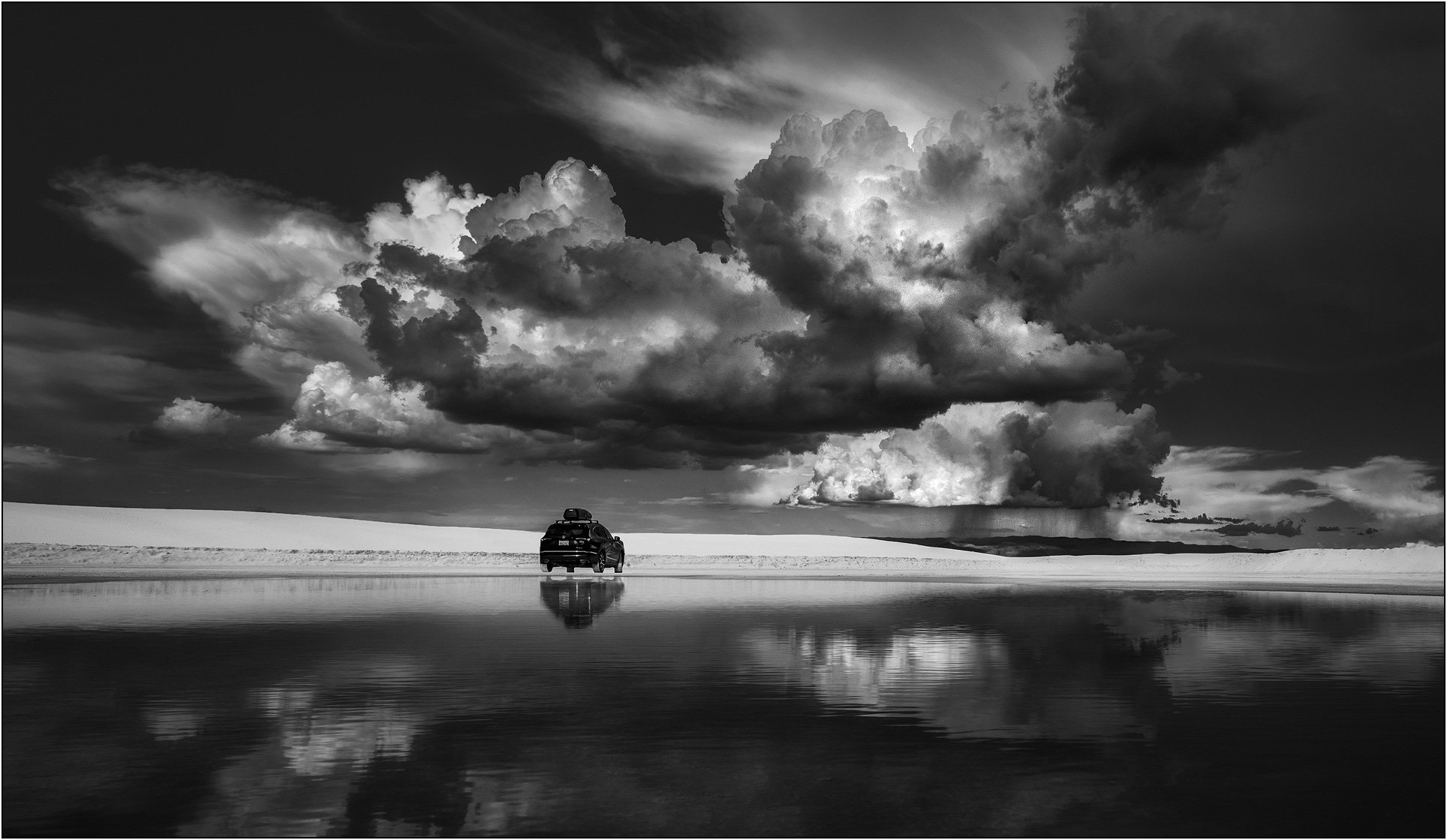 Car driving across reflective water in White Sands with dramatic storm clouds overhead in New Mexico