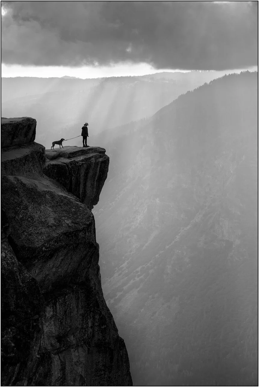 Woman with dog standing on cliff edge overlooking misty mountains in Yosemite National Park