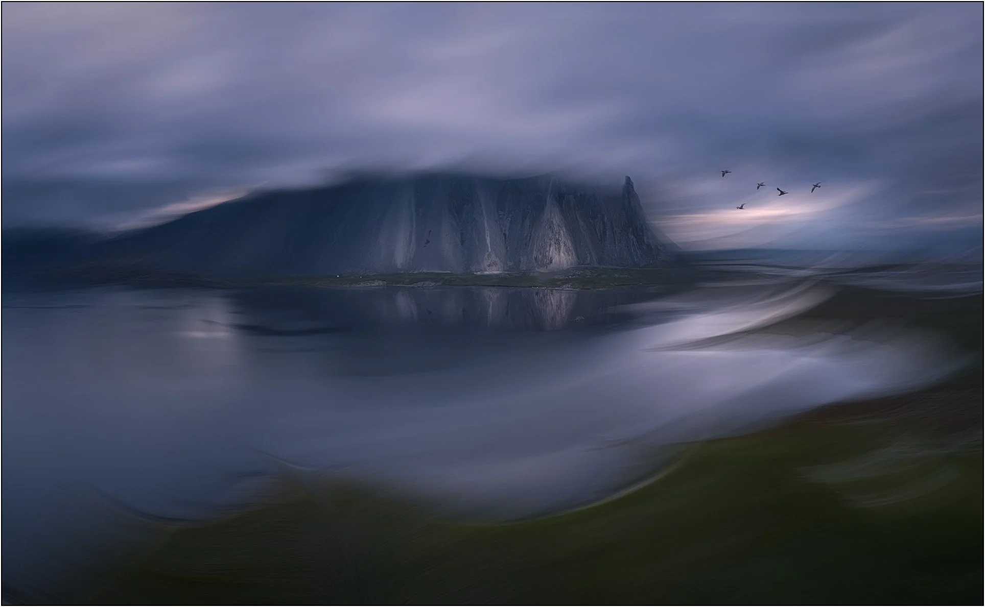 A fog-draped coastal mountain in Iceland, softly blurred into a dreamlike scene with birds crossing the sky.
