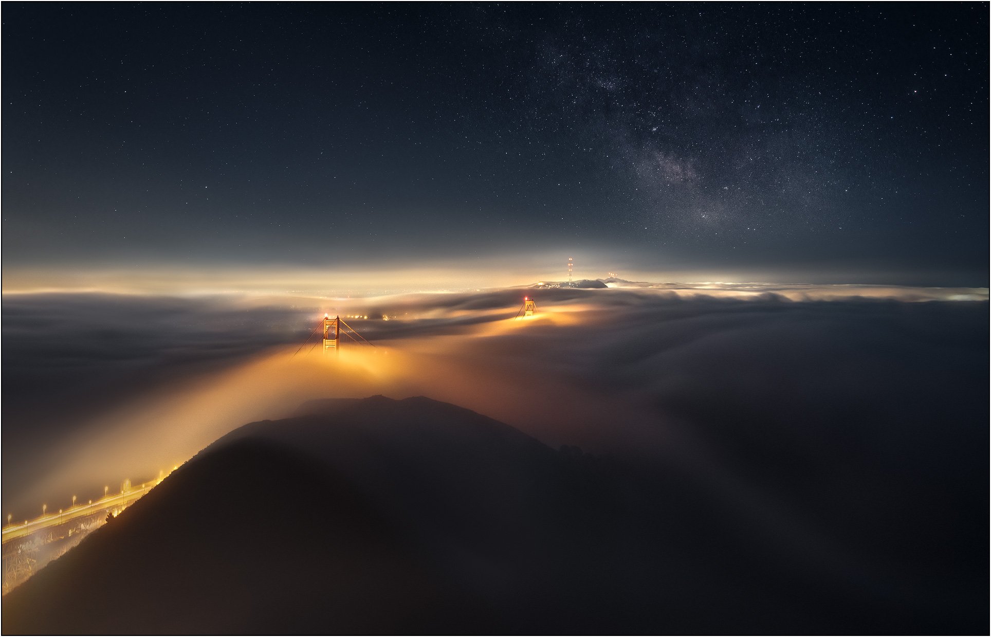 Golden Gate Bridge towers emerging above low fog under milky way