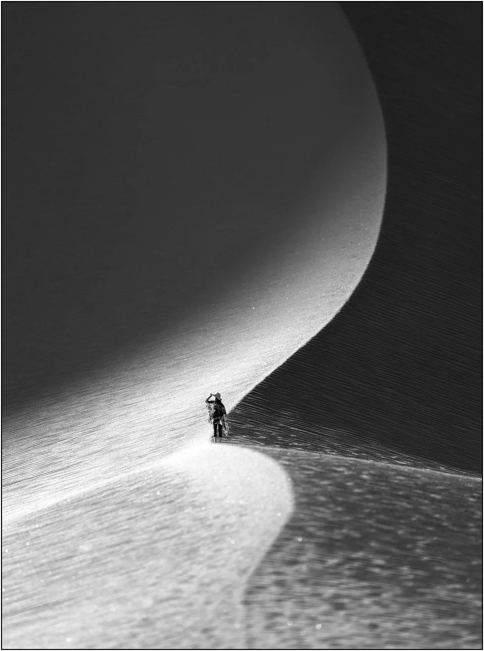 Figure walking along sand dune ridge in high-contrast black and white