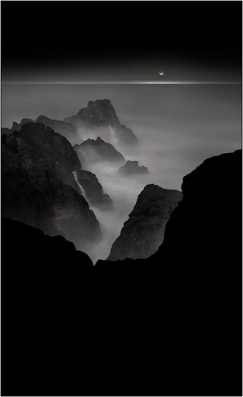 Black and white seascape with rocks emerging through mist and a distant moon above a calm horizon, Monterey, California.