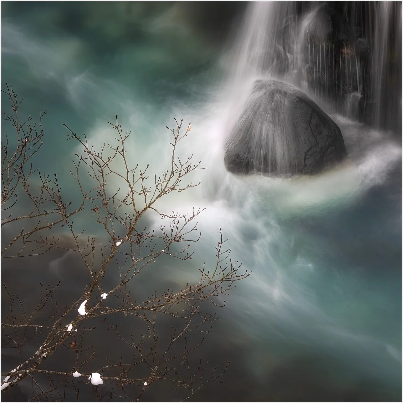 A winter view of Shirahige Waterfall with flowing turquoise water and bare branches in Hokkaido, Japan.