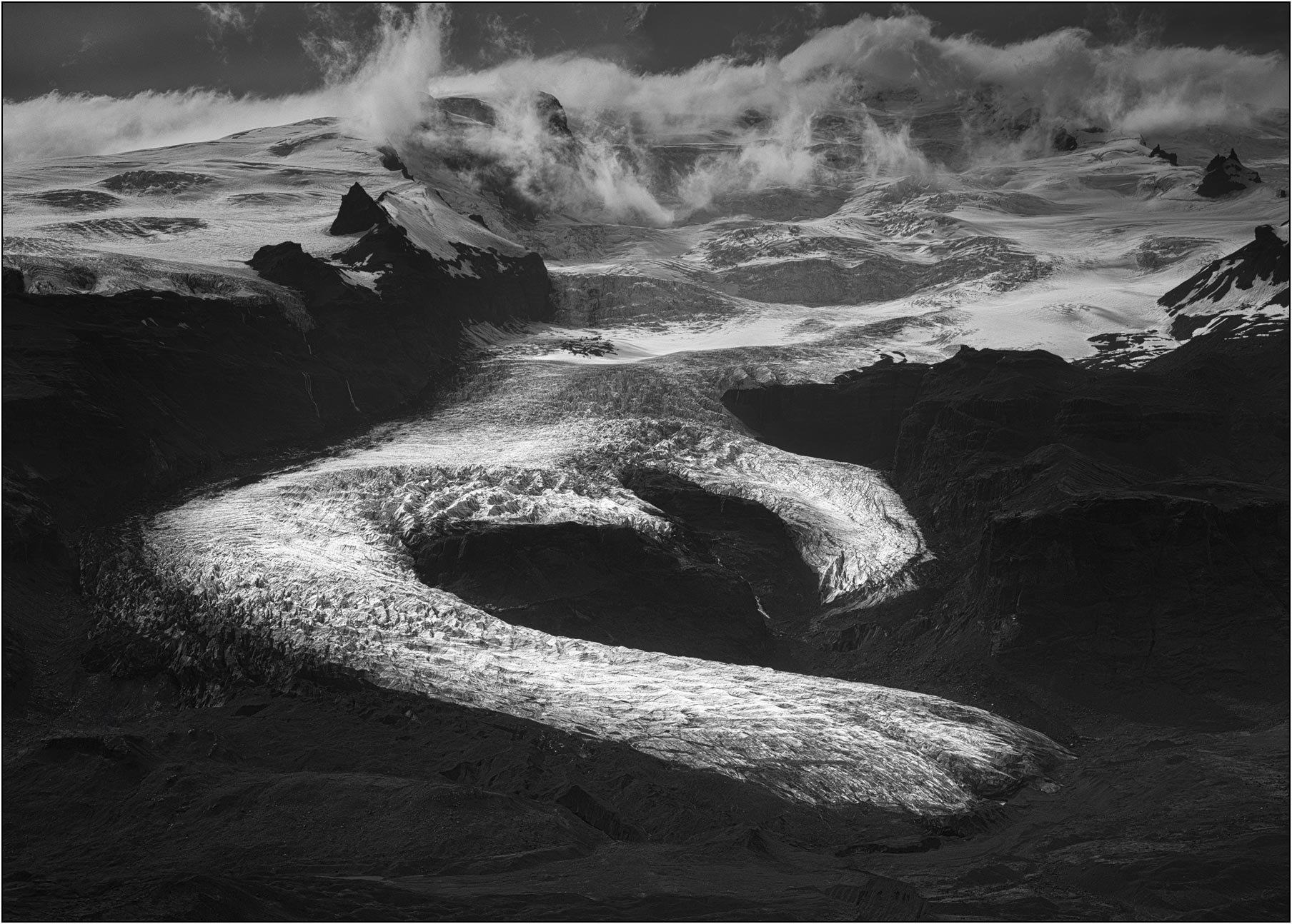 Black and white aerial view of a heart shaped Vatnajökull glacier in Iceland with dramatic clouds.