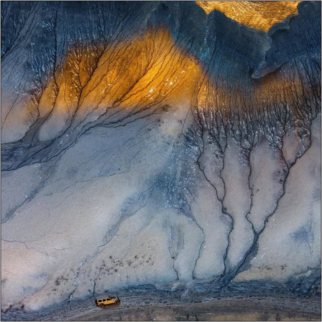 Aerial view of colorful badlands formations with a vehicle for scale in Utah desert