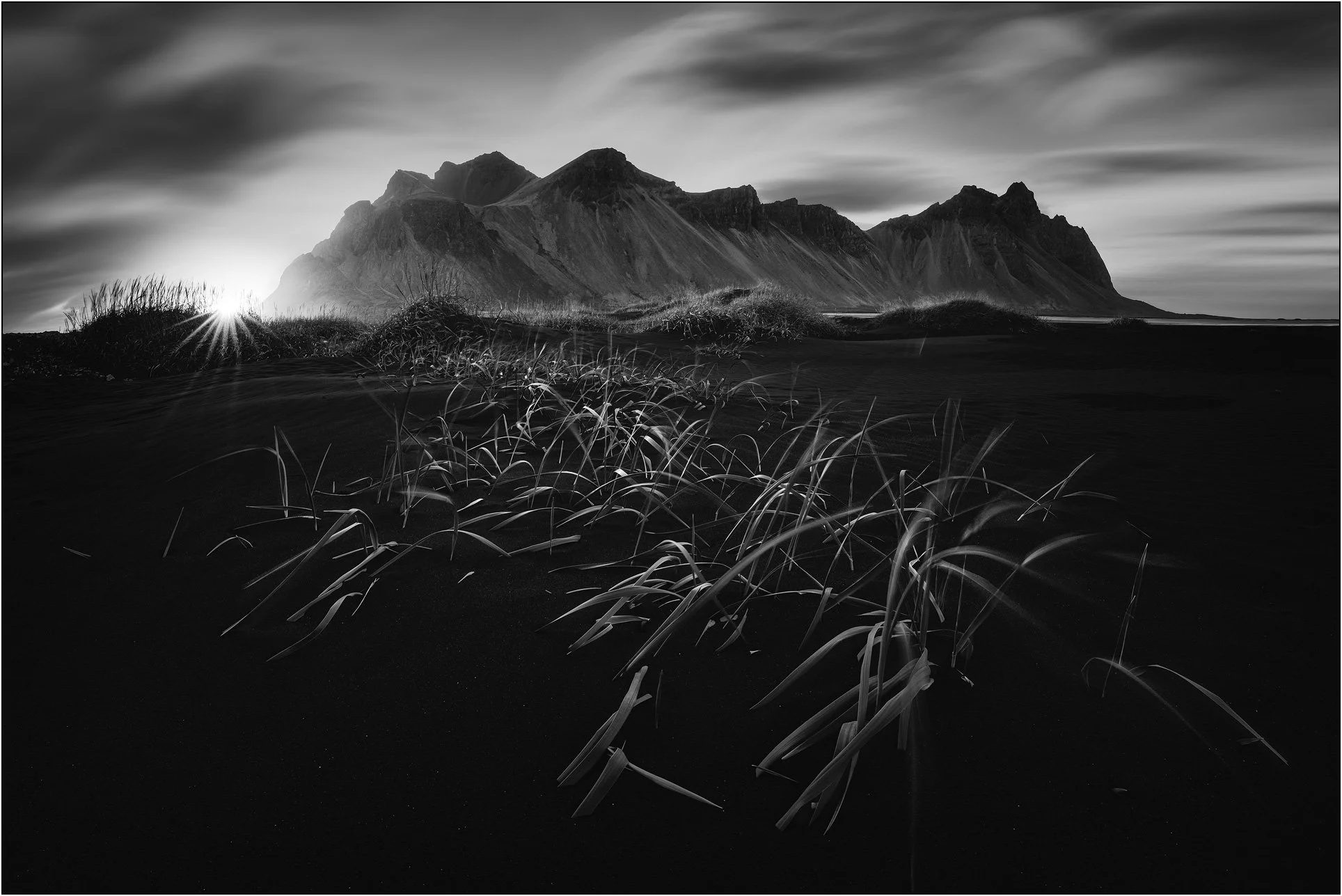 Black and white long exposure landscape image of Vestrahorn, Iceland, with grass and sunstar.